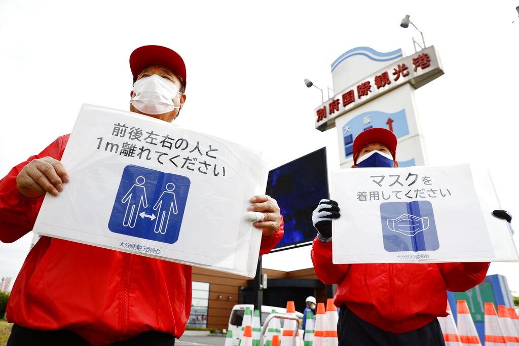 Organizing staff members of the Tokyo Olympic torch relay hold signs urging spectators to wear masks and maintain social distancing in the Oita Prefecture city of Beppu, southwestern Japan, on April 23, 2021, amid the coronavirus pandemic. (Kyodo News/AP Images)