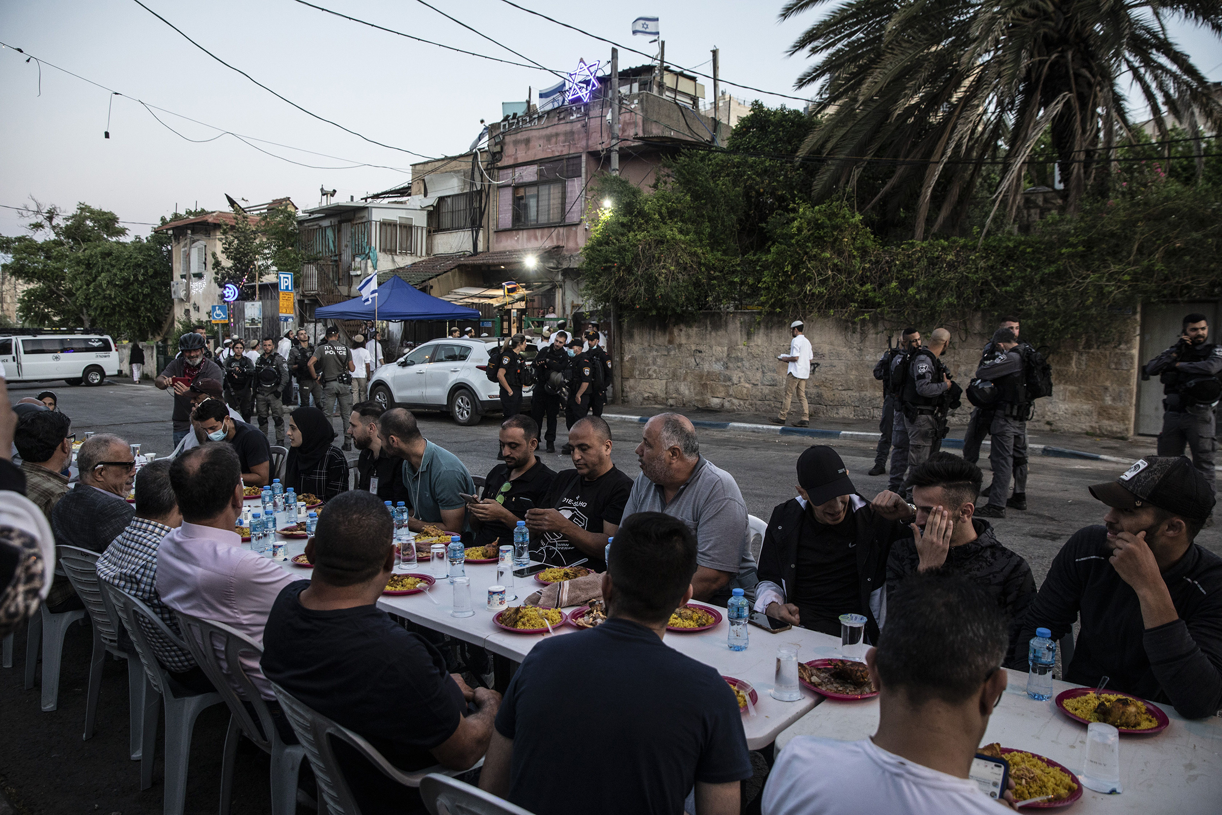 Palestinians sit at a large table to break the fast during Ramadan as Israeli border police guard Jewish settlers, outside one of the homes they have taken over from a Palestinian family and by other homes of Palestinians facing eviction, in the East Jerusalem neighborhood of Sheikh Jarrah on May 7, 2021.