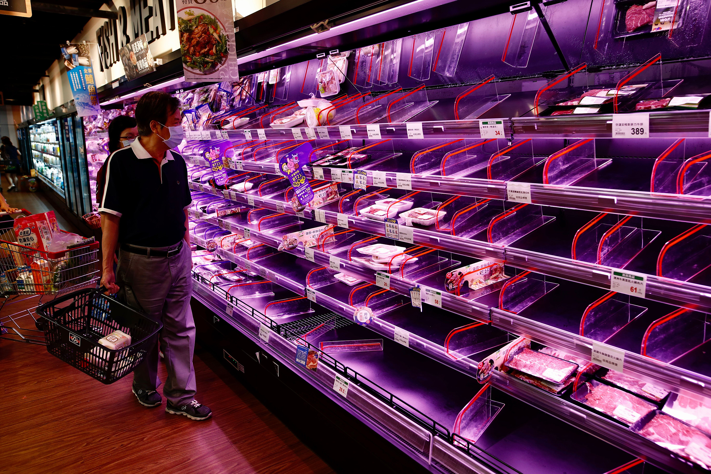 Shoppers check largely empty shelves of meat as they rush to buy grocery essentials inside a supermarket in Taipei on May 17, 2021.