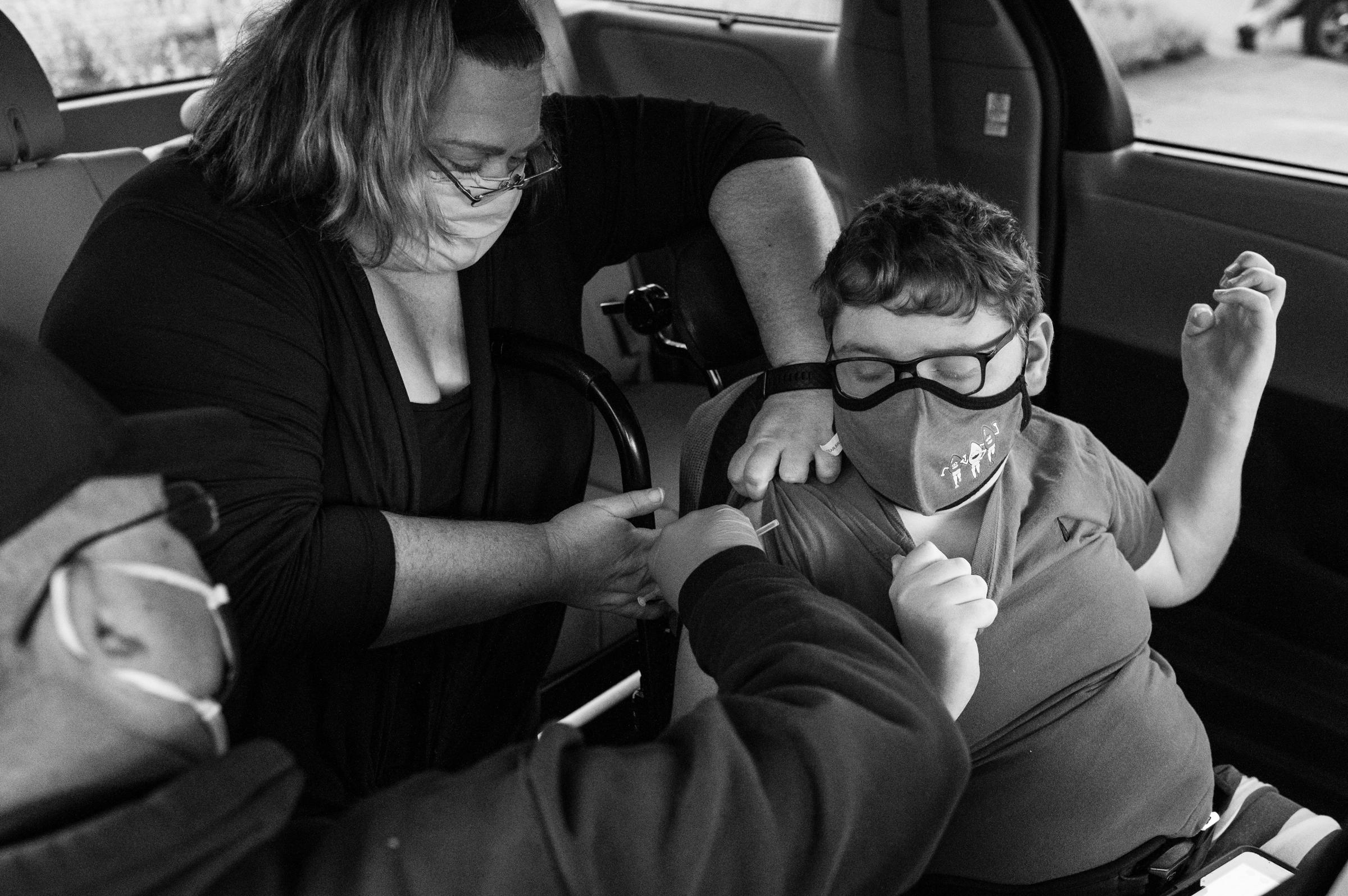 Allison Bungard of Charleston lifts the shirt of her son Andrew, 13, who has cerebral palsy and Factor V Leiden thrombophilia, while he receives his CoVid-19 vaccination at Bible Center Church on June 4, 2021 in Charleston, West Va.