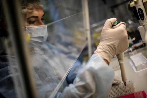 A laboratory technician wearing protective equipment works on the genome sequencing