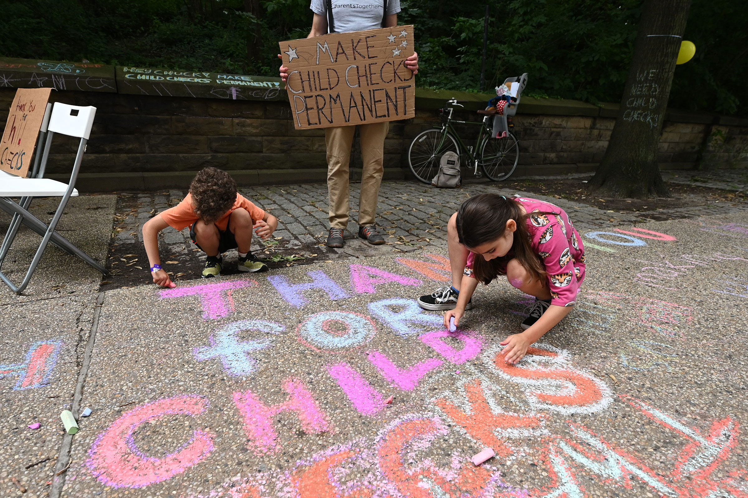 Justin Ruben, Rime Leonard and  Edie Abrams-Pradt draw with chalk to celebrate new monthly Child Tax Credit payments and urge congress to make them permanent outside Senator Schumer's home on July 12, 2021 in Brooklyn, New York. (Bryan Bedder—Getty Images/ParentsTogether)