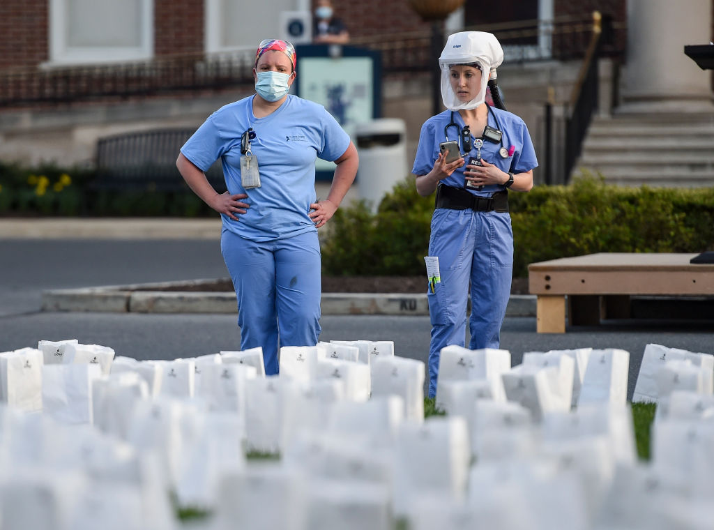 Two healthcare workers in PPE look at the memorial outside the hospital. At the Reading Hospital in West Reading, Penn., Thursday evening April 8, 2021 where the Hospital held a Memorial ceremony for the 938 Berks County Residents who have died from COVID-19. Luminaries were setup for each person who died. (Ben Hasty–MediaNews Group/Reading Eagle/Getty Images)
