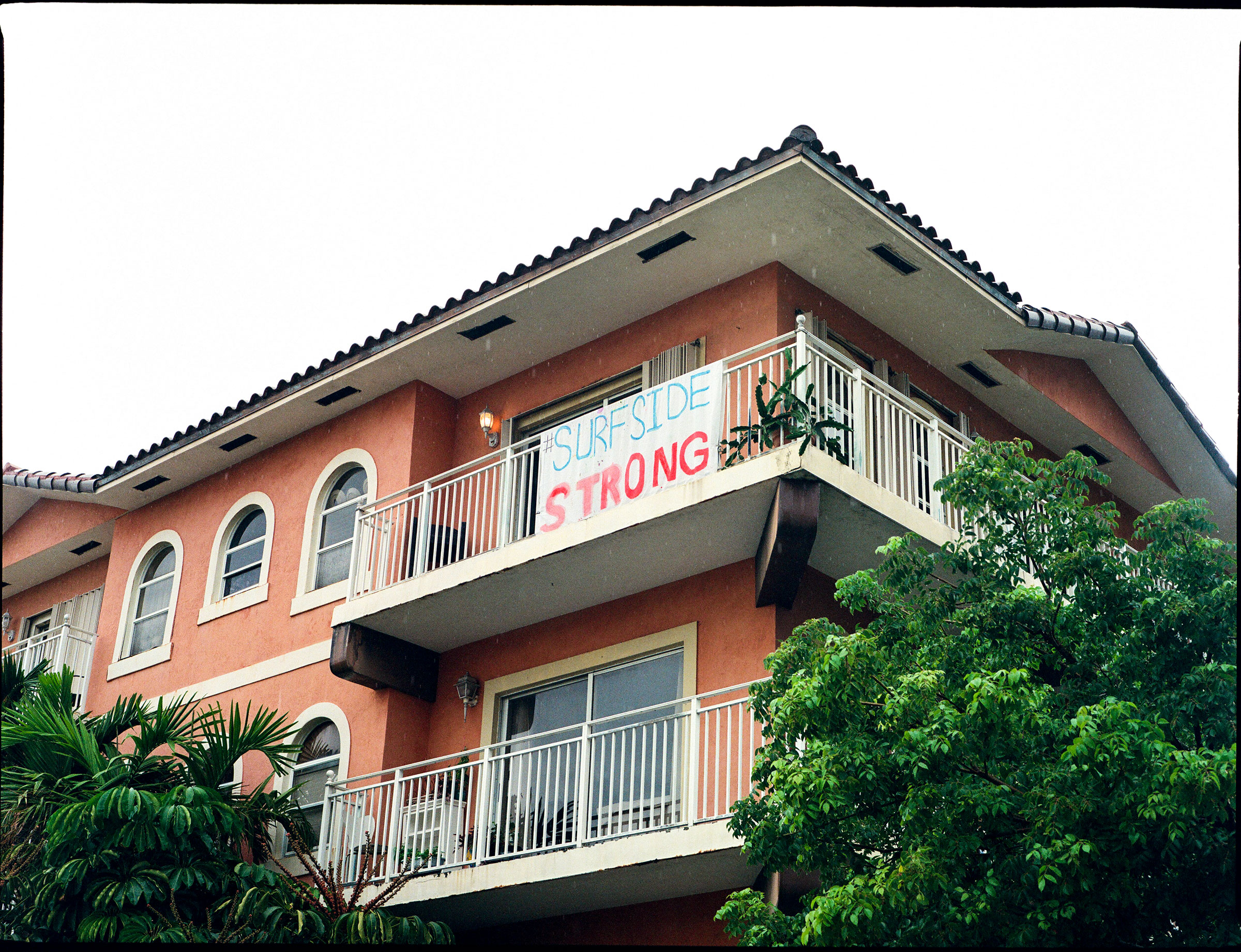 A sign hangs off of the balcony of a nearby apartment building that reads "Surfside Strong".