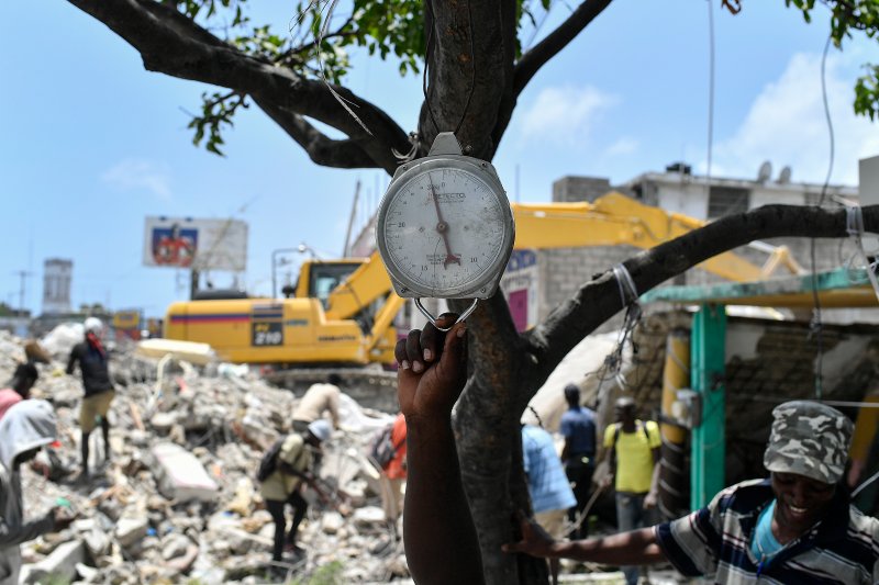 A vendor holds onto a scale as he waits for scavengers to bring him found metal pieces to weigh, at the site of a home that was destroyed by last week's 7.2 magnitude earthquake, in Les Cayes, Haiti, on Aug. 21, 2021.