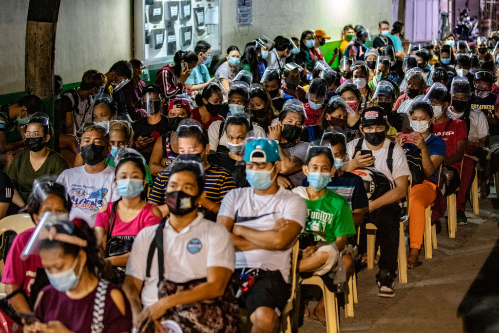 People hoping to get vaccinated against COVID-19 sit while queuing outside a vaccination site on August 08, 2021 in Las Pinas, Metro Manila, Philippines. (Ezra Acayan-Getty Images)