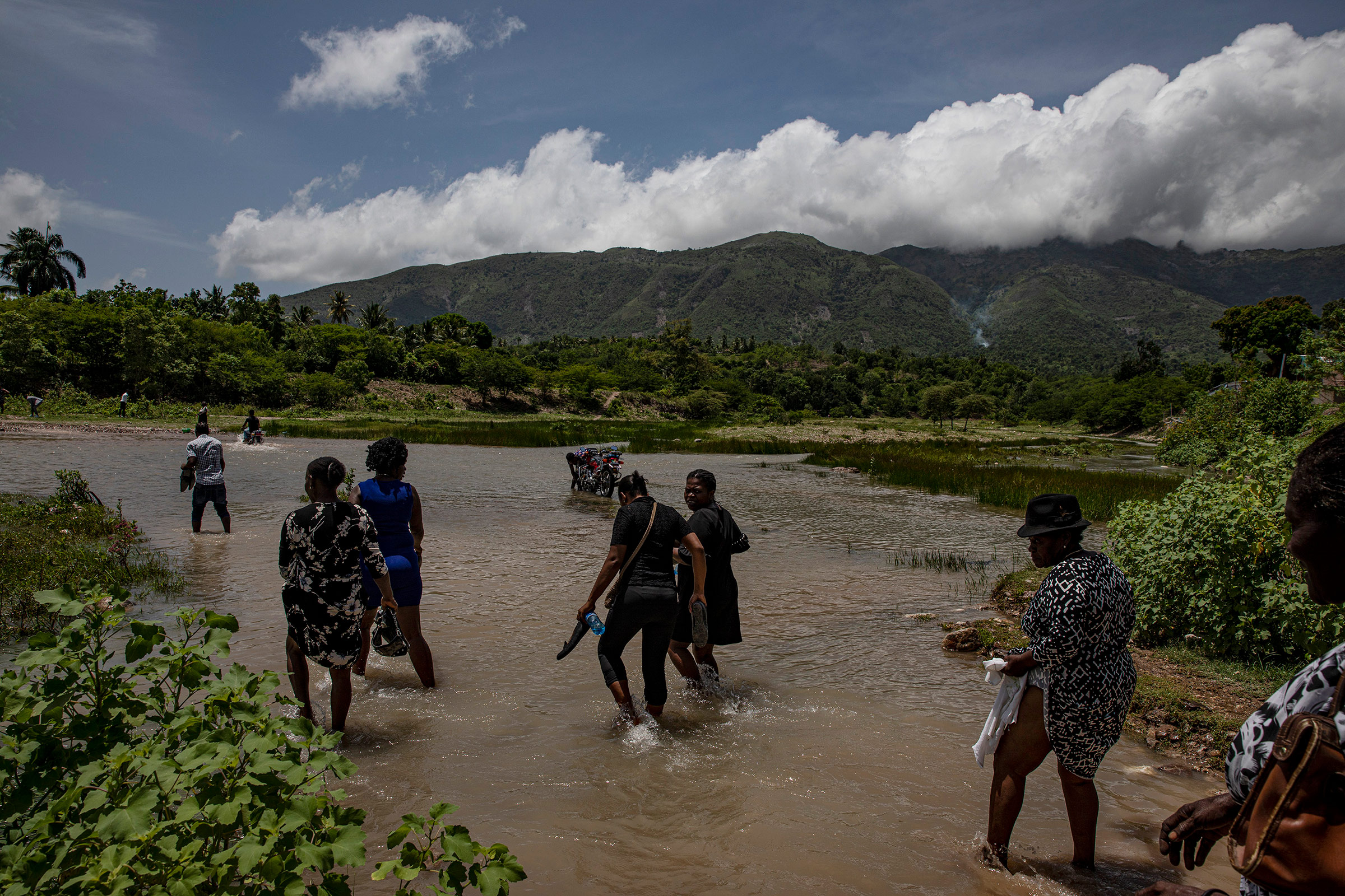 People cross a river during a funeral procession for a person who died during the earthquake in L'Asile on Aug. 18.