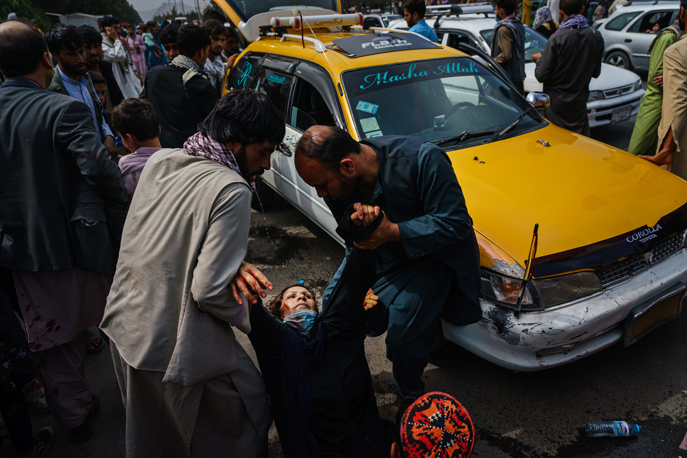 Men try to help a wounded woman and her child, who was also injured, after Taliban fighters use gunfire, whips, sticks and sharp objects to maintain control over a crowd of thousands waiting outside the airport in Kabul on Aug. 17, 2021.
