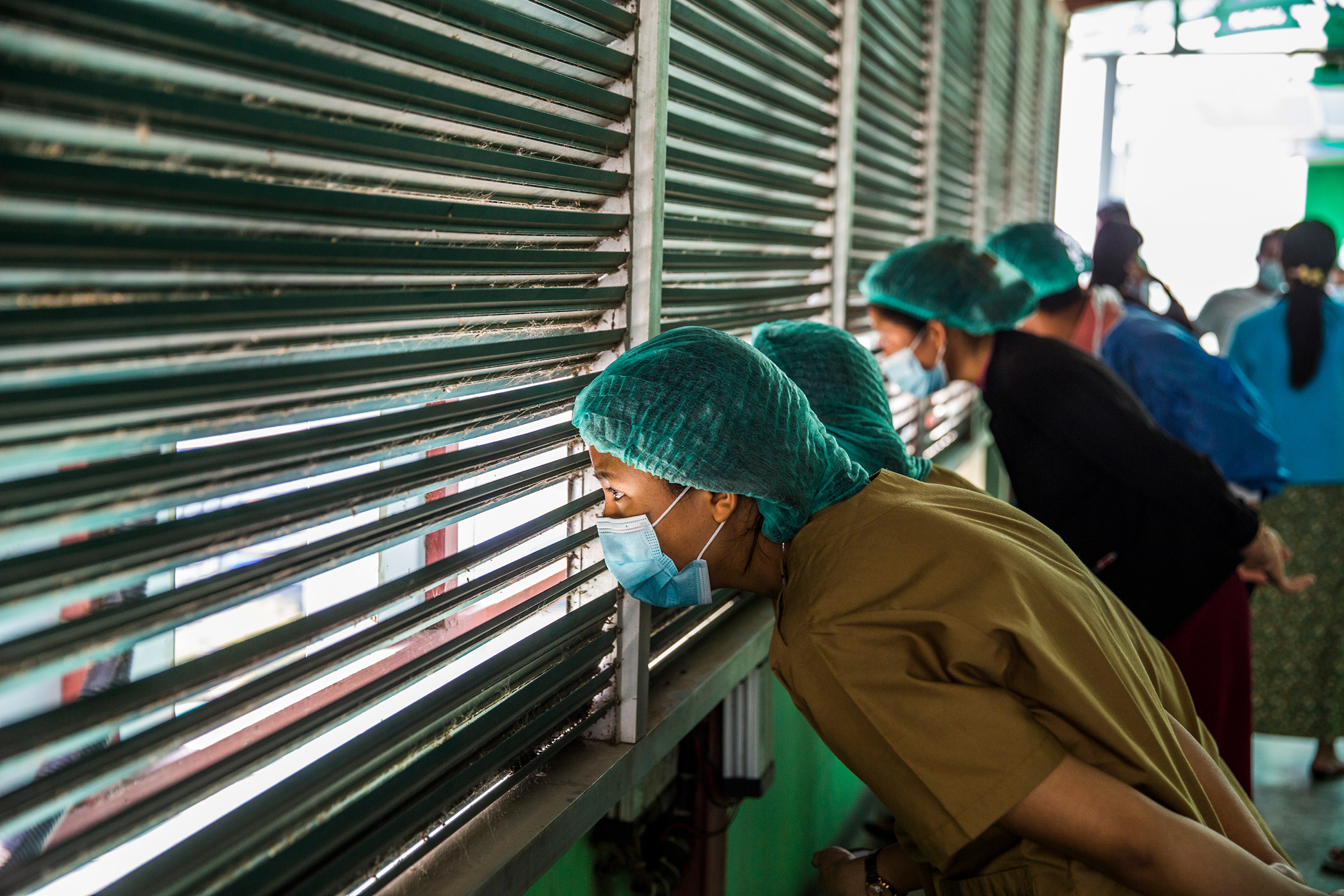 Health care workers watch protesters demonstrate against Myanmar's military coup in Myanmar's capital of Yangon, Feb. 28. (The New York Times)