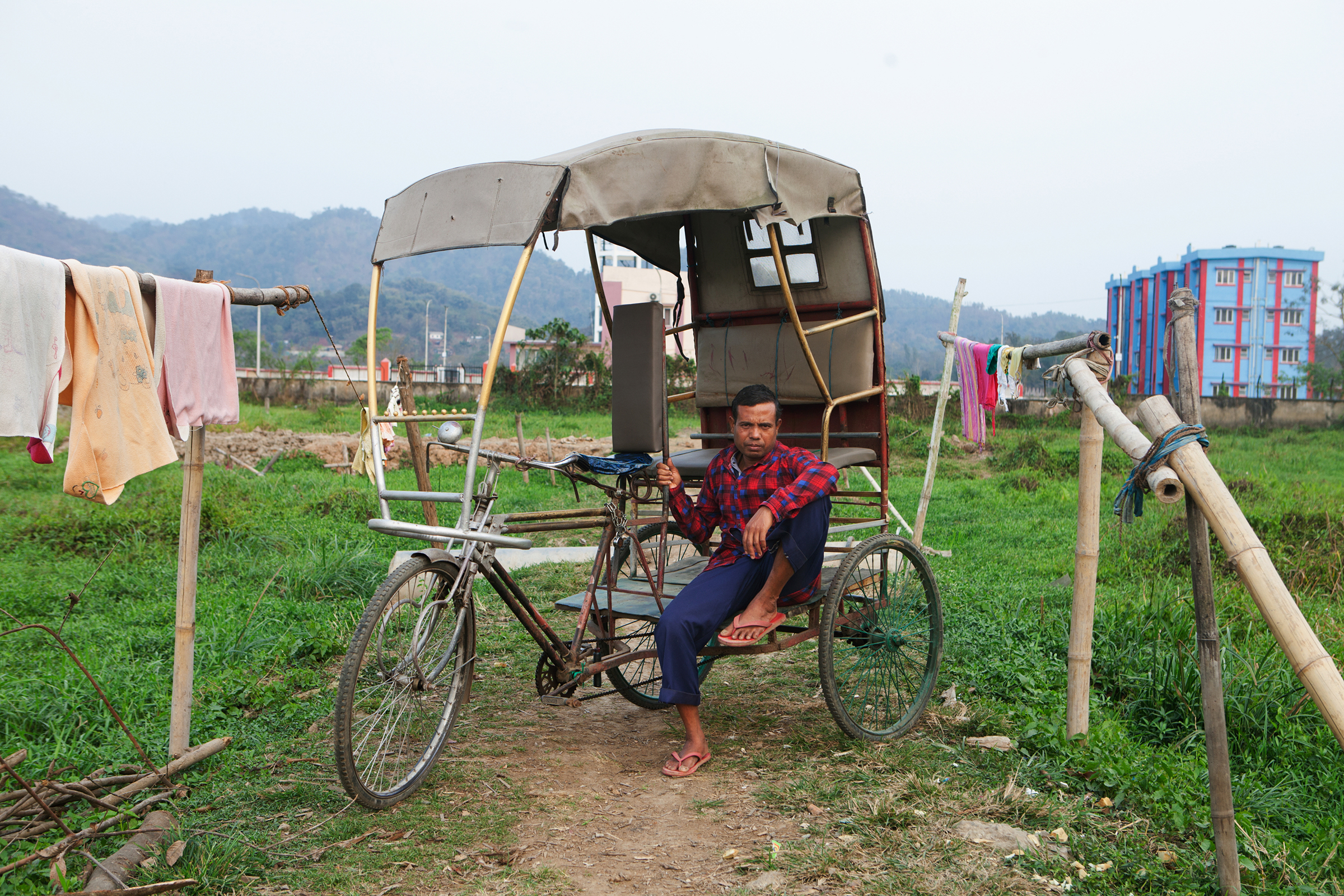 Nur Hussein rests on his rickshaw in a field adjacent to his home.