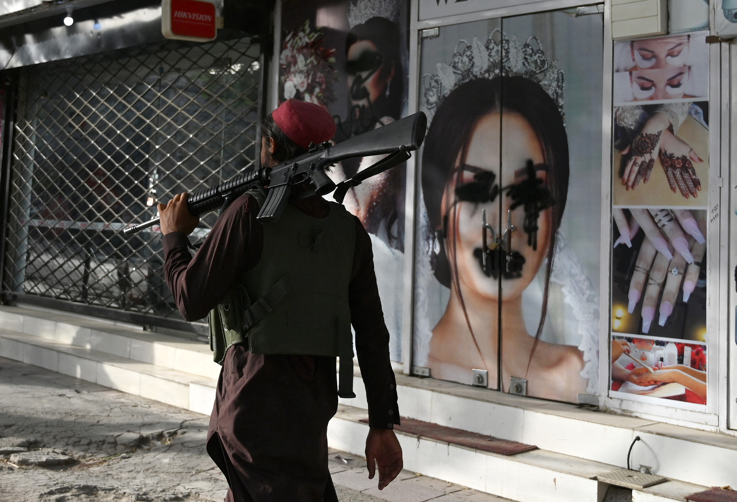 A Taliban fighter walks past a beauty salon with images of women defaced using spray paint in the Shar-e-Naw area of Kabul on Aug. 18. (Wakil Kohsar—AFP/Getty Images)