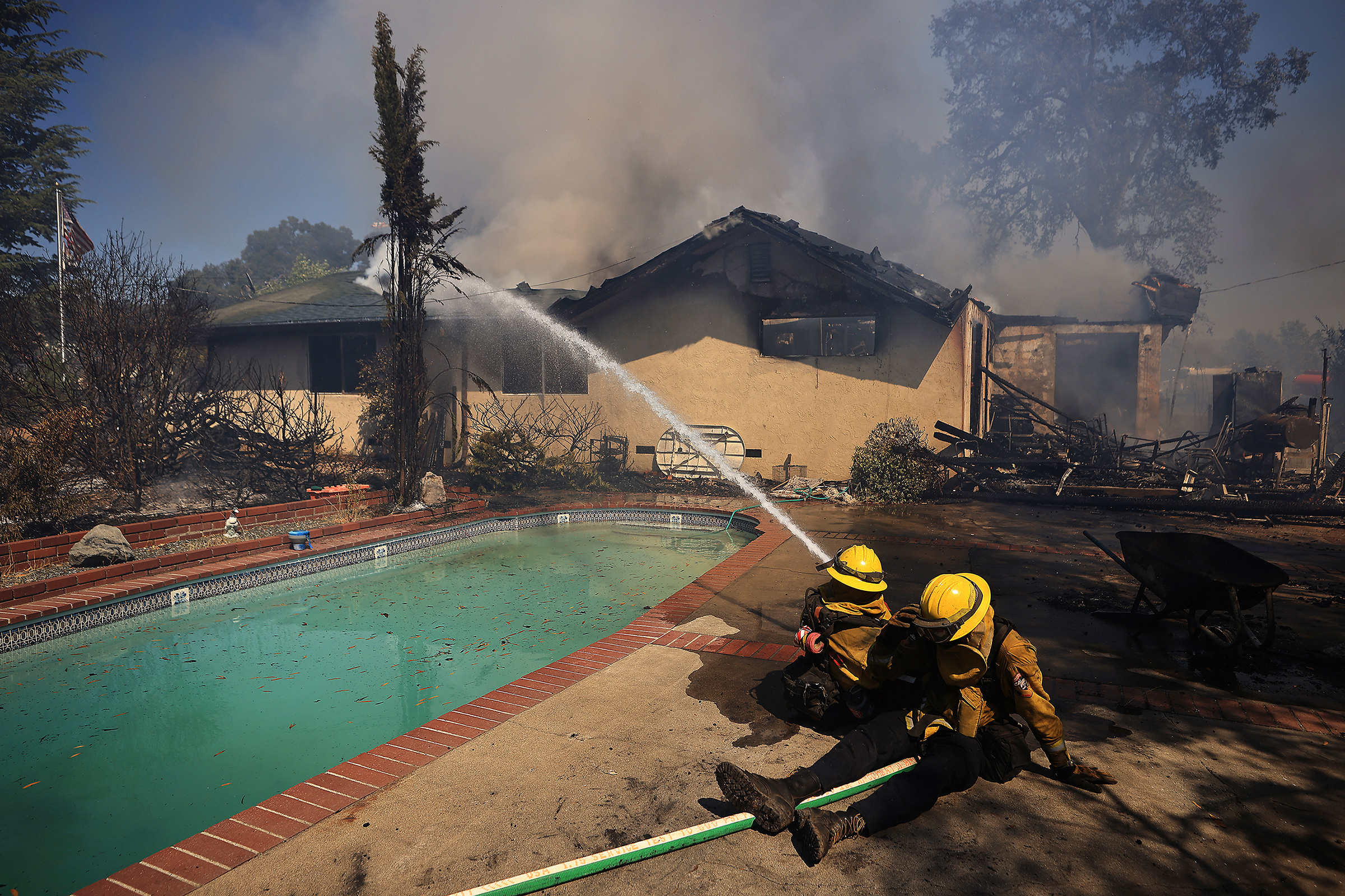 Firefighters take a defensive stand against a home burning in Redwood Valley, Calif., ignited by an 80 acre wind whipped brush fire fed by tinder dry conditions on July 7. (Kent Porter—The Press Democrat/AP)