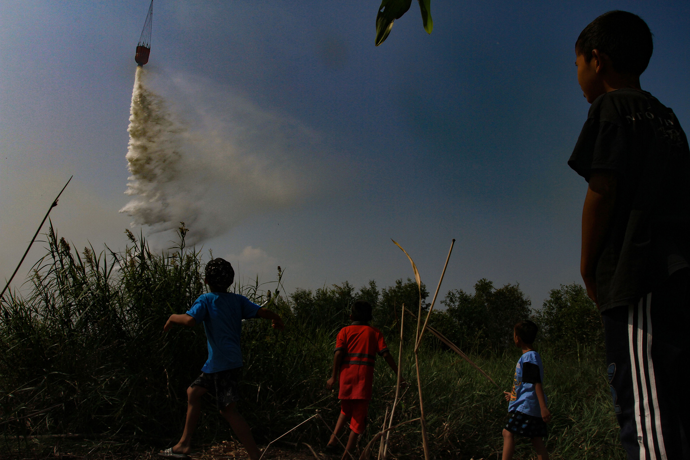 Children watch a helicopter dumping water on burning peatland at Palem Raya village in Ogan Ilir district, South Sumatra, Indonesia, on July 31