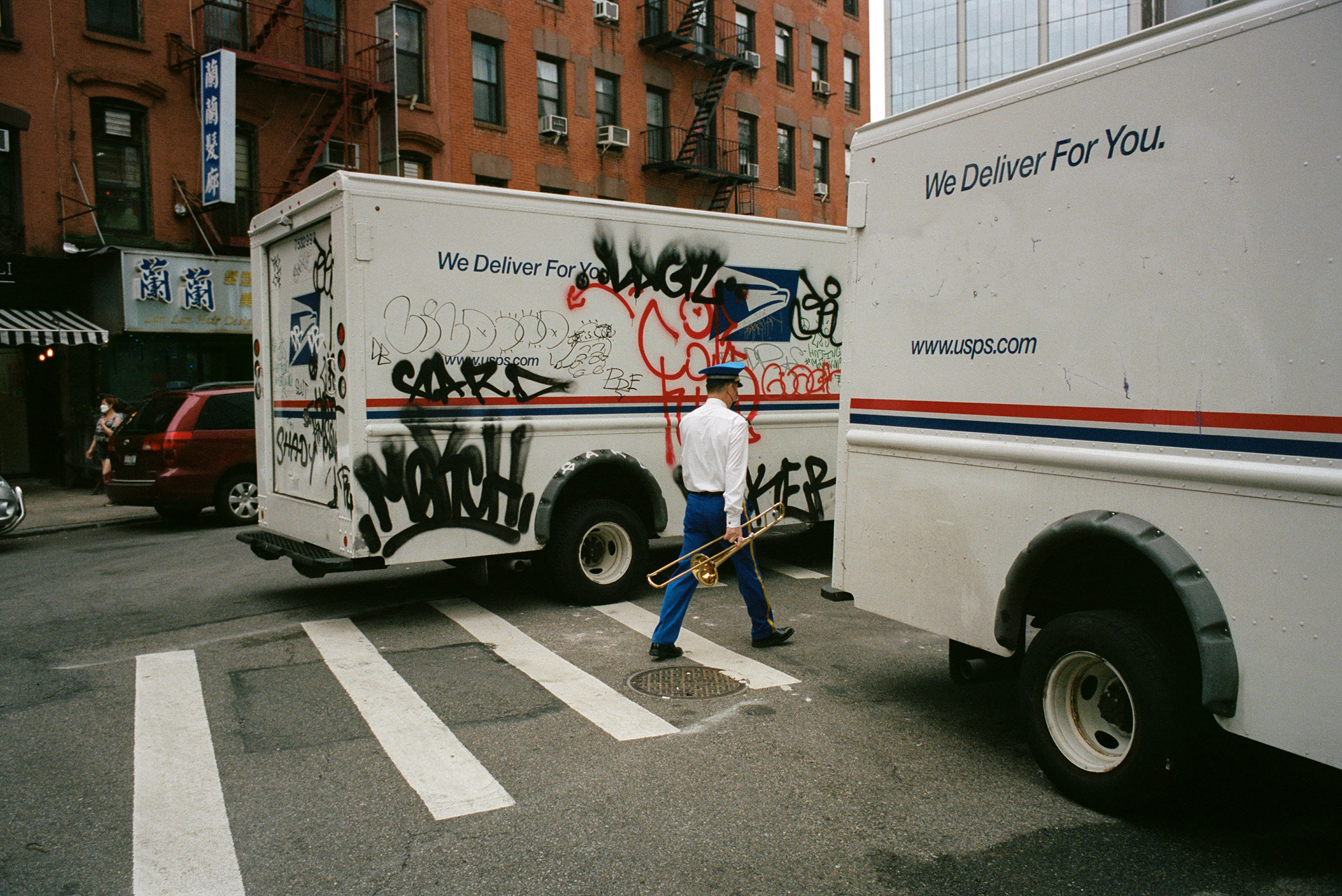 A trombonist from a Chinatown funeral band slips between mail trucks, Sept. 4, 2021. (Daniel Arnold for TIME)