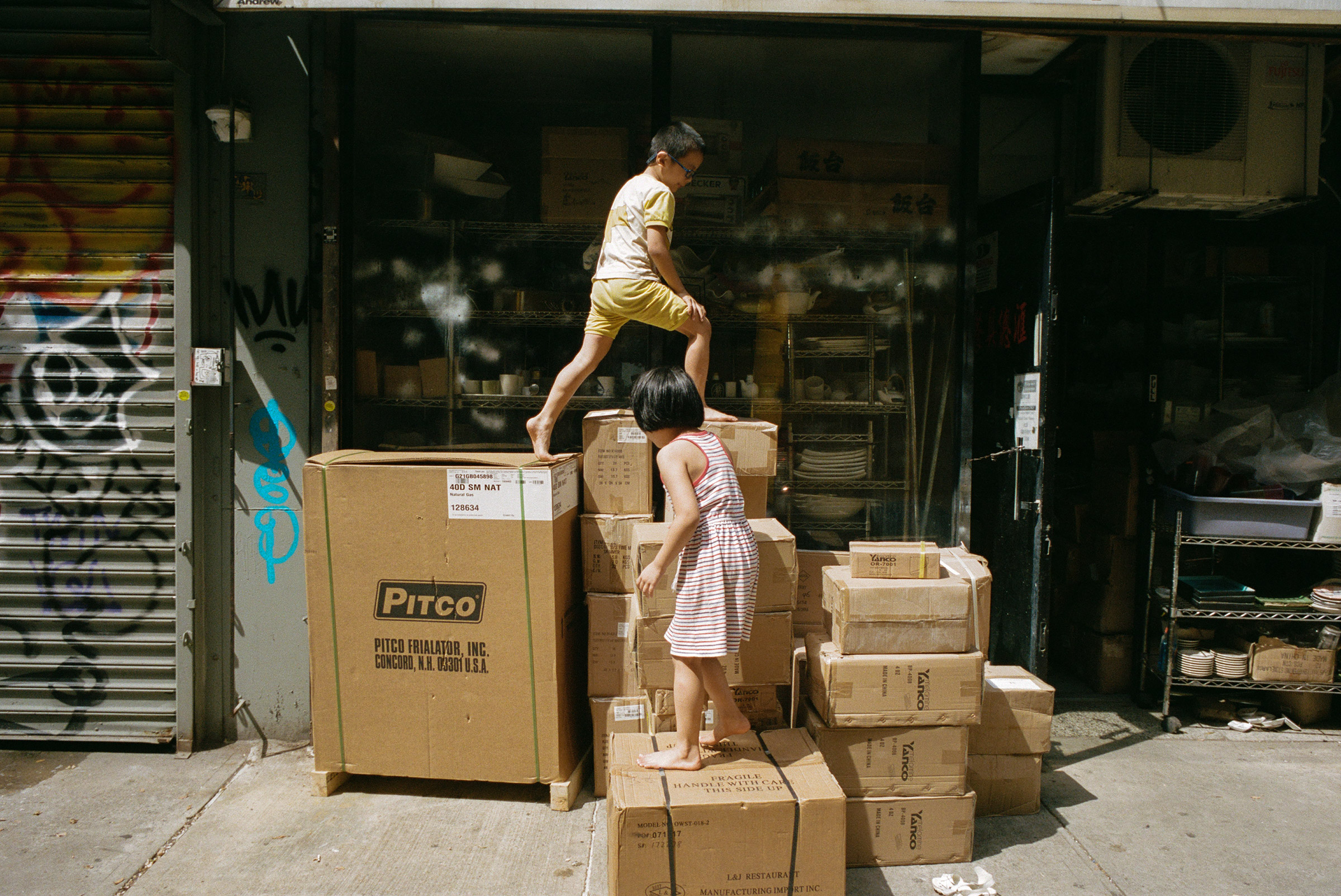 Kids climb on stacks of boxed kitchenware at the corner of Ludlow and Hester Streets, Sept. 1, 2021. (Daniel Arnold for TIME)