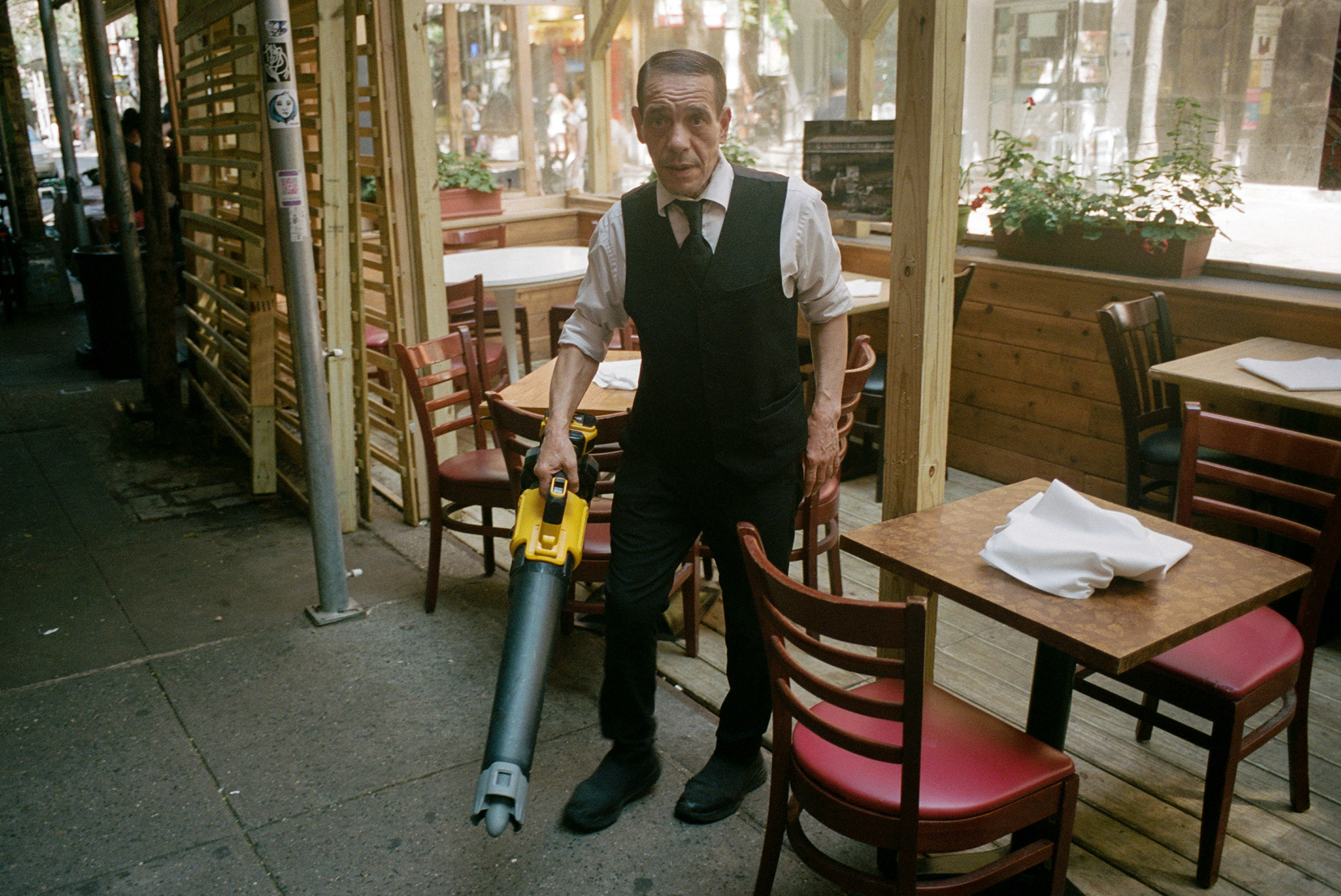 A maître d' cleans an outdoor seating area with a blower before evening service on MacDougal Street, Aug. 12, 2021. (Daniel Arnold)