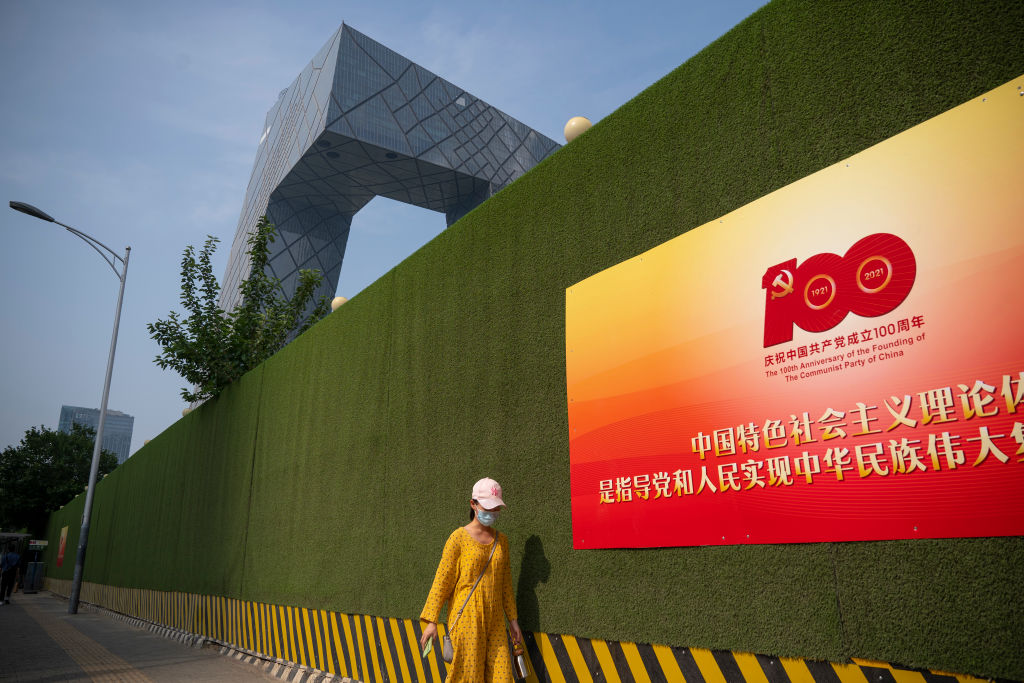 A woman walks past a sign celebrating the centenary of the Communist Party of China, with the CCTV headquarters seen in the background, on June 28, 2021 in the central business district of Beijing. (Andrea Verdelli/Getty Images)