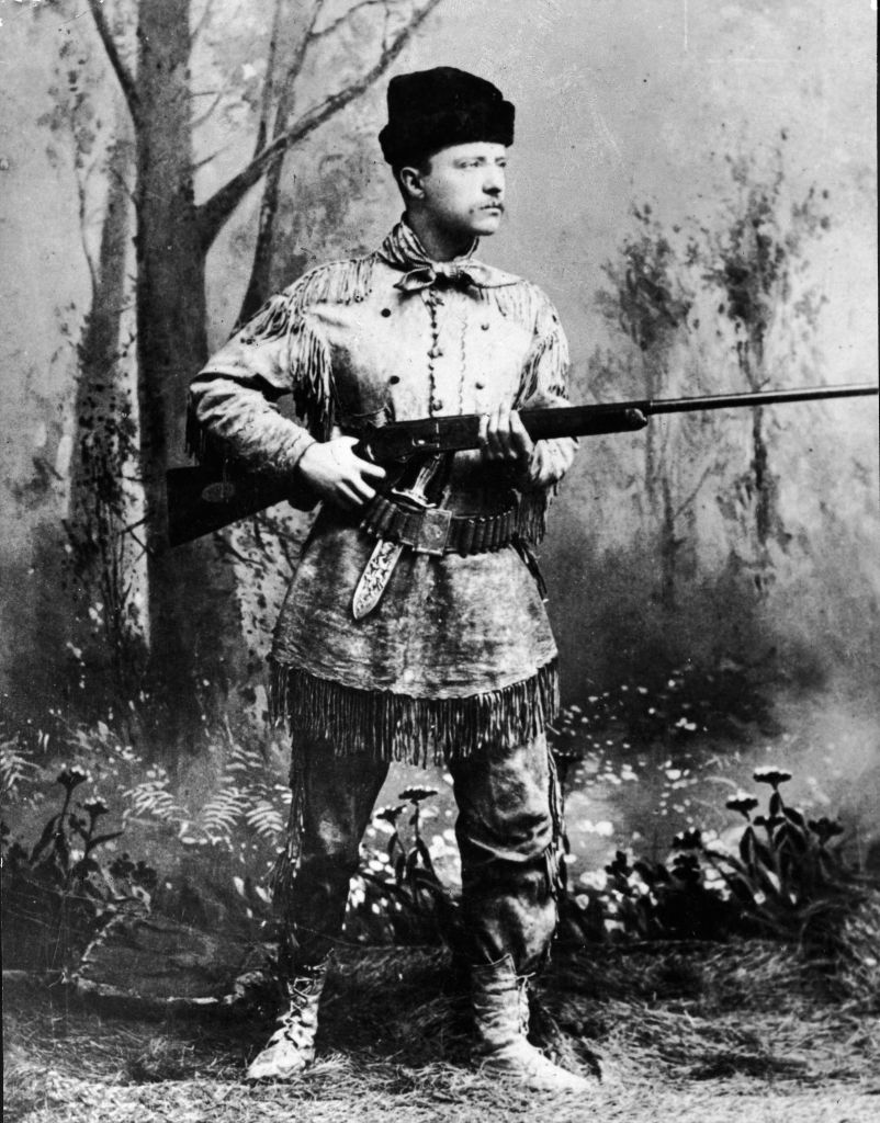 A full-length studio portrait of Theodore Roosevelt (1858 - 1919), president of the United States from 1901 to 1909, wearing hunting gear and holding a Winchester gun in an artificial forest setting, circa 1900. (Pictorial Parade/Getty Images)