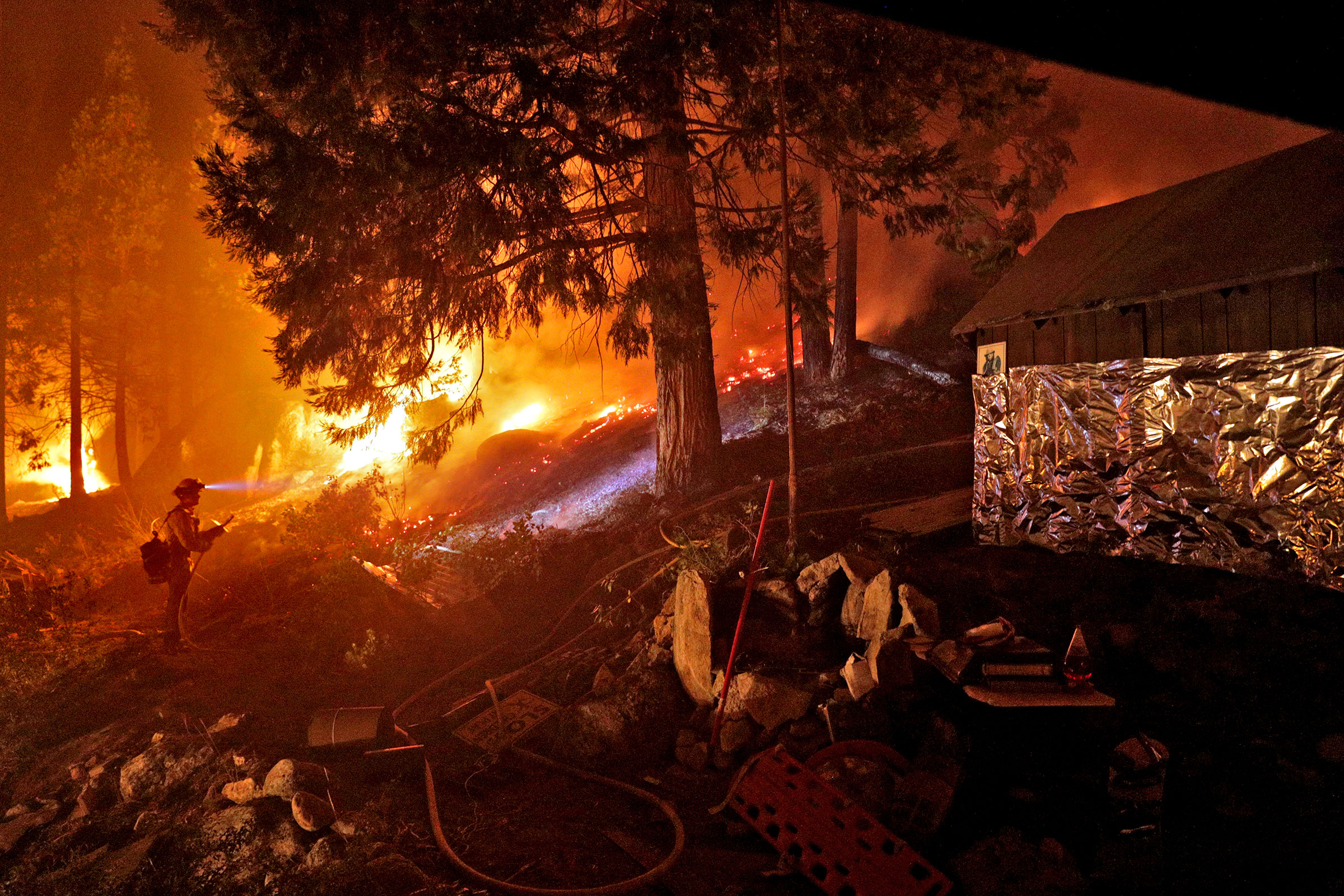 A firefighter monitors a back burn along Highway 50 next to a home that was partially wrapped in foil as crews continued structure prevention at the Caldor Fire in Strawberry, Calif., on Sunday, August 29, 2021. (Carlos Avila Gonzalez—San Francisco Chronicle/Getty Images)