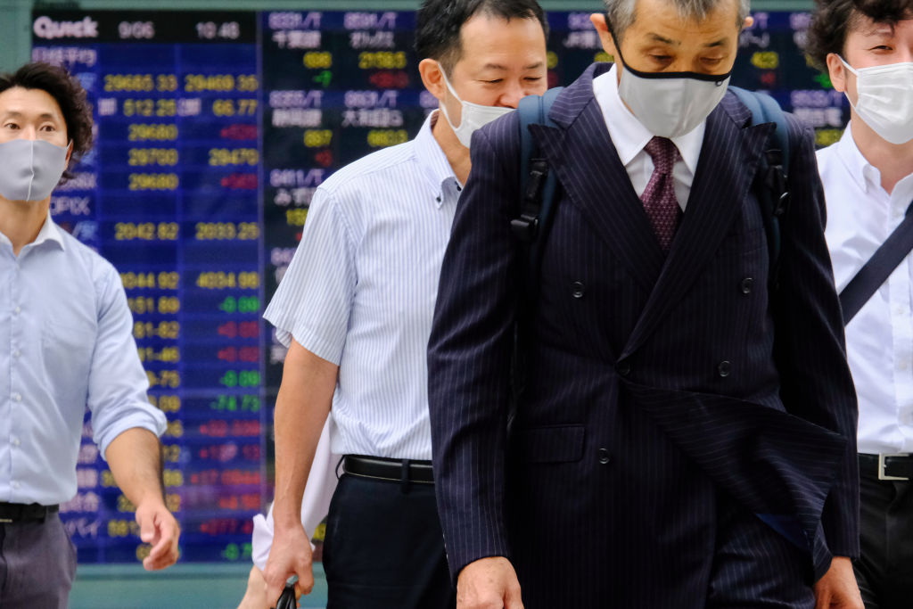 Japanese businessmen walk past a screen displaying Nikkei