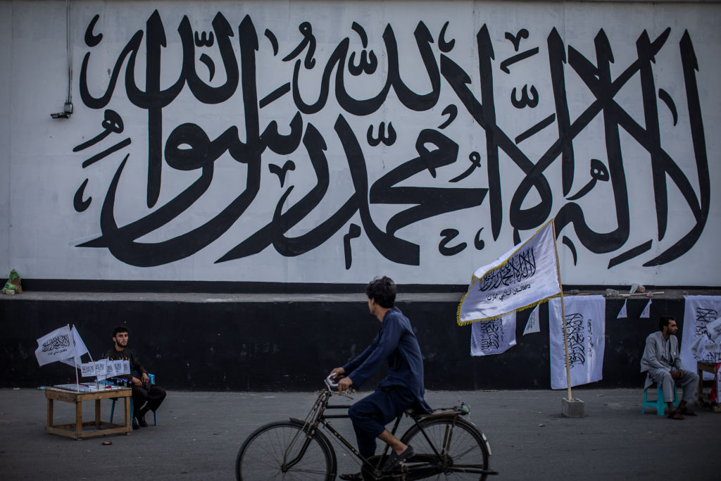 Afghan men sell Taliban flags backdropped by the Muslim creed written on a wall of the former United States embassy in Kabul, Afghanistan, on September 24, 2021. (Oliver Weiken—Getty Images)