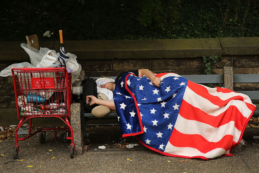 A homeless man sleeps under an American Flag blanket on a park bench on September 10, 2013 in the Brooklyn borough of New York City. (Photo by Spencer Platt/Getty Images)