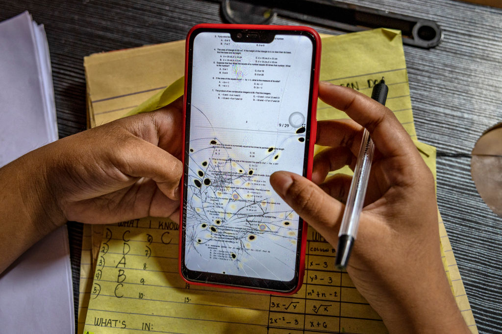 Charilyn Caparas, a grade 8 student, views lessons on her phone with a cracked screen while studying at home as schools remain closed on October 13, 2021 in the coastal village of Pamarawan in Malolos, Bulacan province, Philippines. (Ezra Acayan/Getty Images)