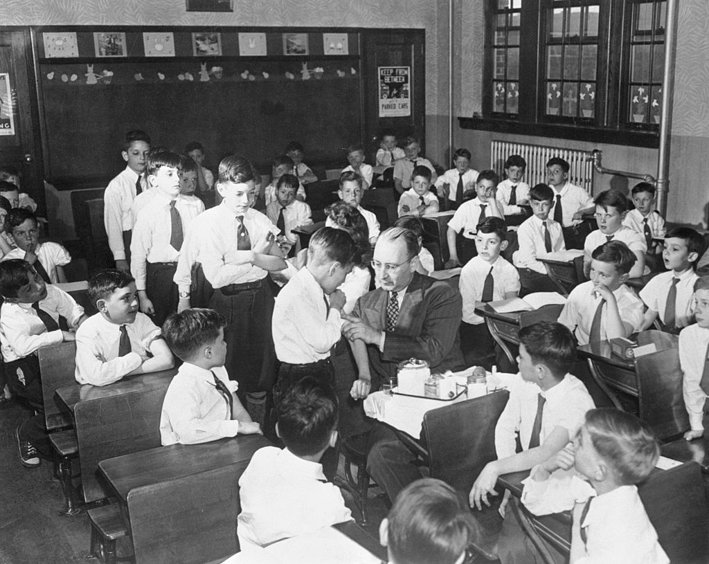 Dr. George Long, vaccinates little Patrick Hogan, while other children in the class line up awaiting their turn at the needle on April 14, 1947. This scene was taken at the St. Joan of Arc, parochial school in Jackson Heights, Queens. (Bettmann Archive)