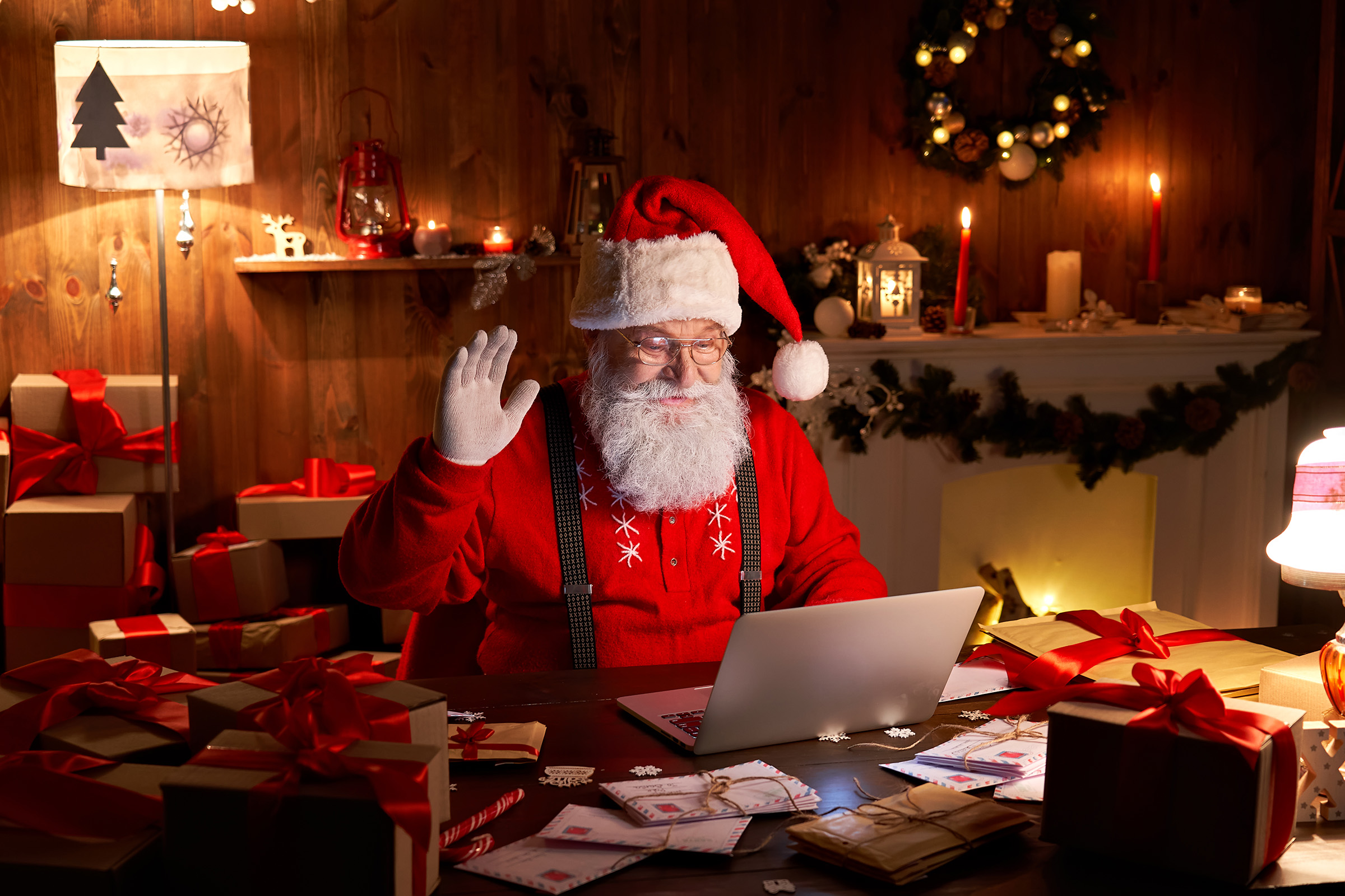 Happy Santa Claus waving handÂ  video calling kid talking to child greeting on Merry Christmas, Happy New Year in virtual video online chat on laptop sitting at home table late with present on xmas eve.