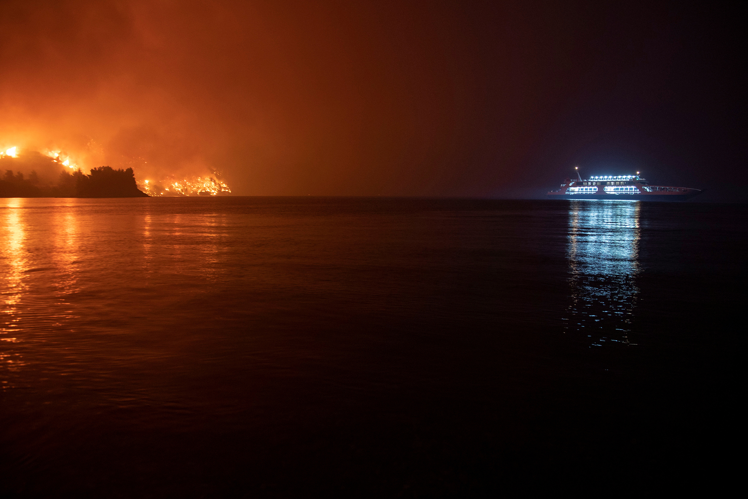 People are evacuated on a ferry as a wildfire burns in the Greek village of Limni, on the island of Evia, on Aug. 6. With other escape routes blocked by flames, residents and tourists had been urged to flee by boat.