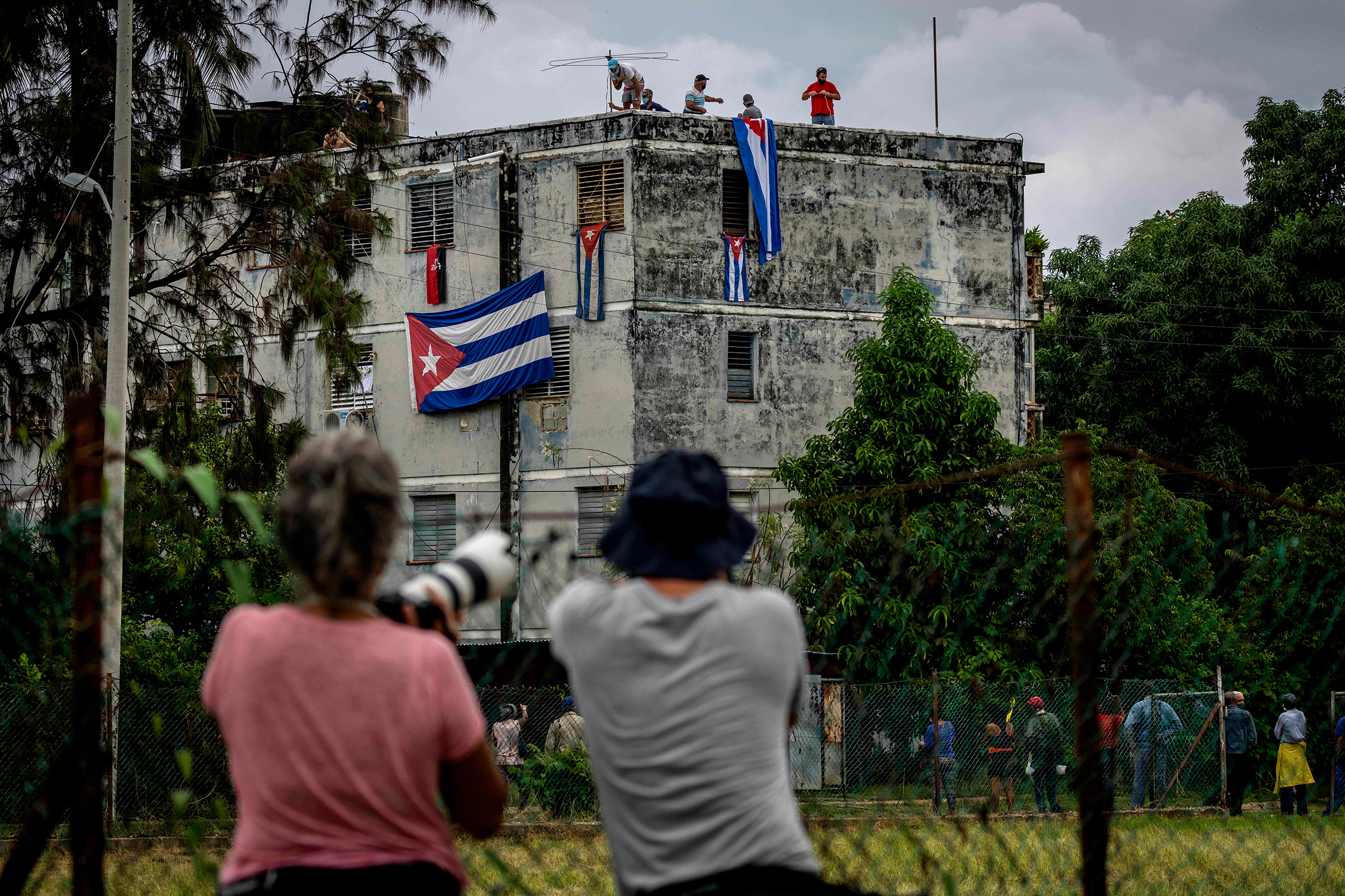 Men hang Cuban flags over the windows of Yunior Garcia Aguilera's home in an attempt to stop him from communicating with the outside on Nov. 14, 2021. García is a playwright and leader of Archipelago, a Cuban opposition group. (Ramon Espinosa—AP)