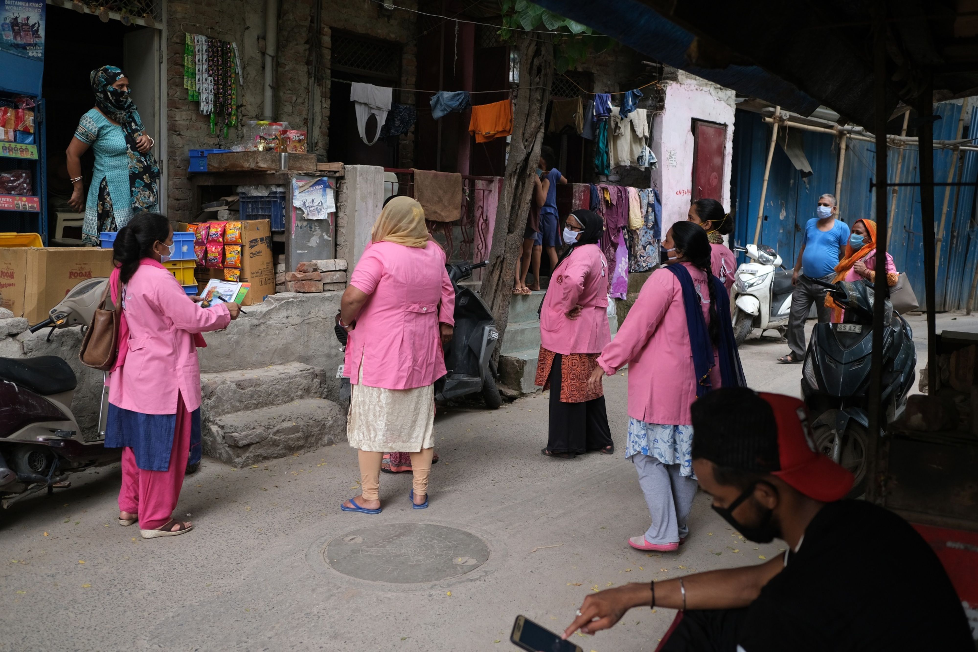 Accredited Social Health Activist (ASHA) workers from India's National Rural Health Mission wearing pink robes and protective masks, talk to a resident, left, as they conduct a door-to-door survey on the coronavirus in New Delhi, India, on July 2, 2020. (© 2020 Bloomberg Finance LP)