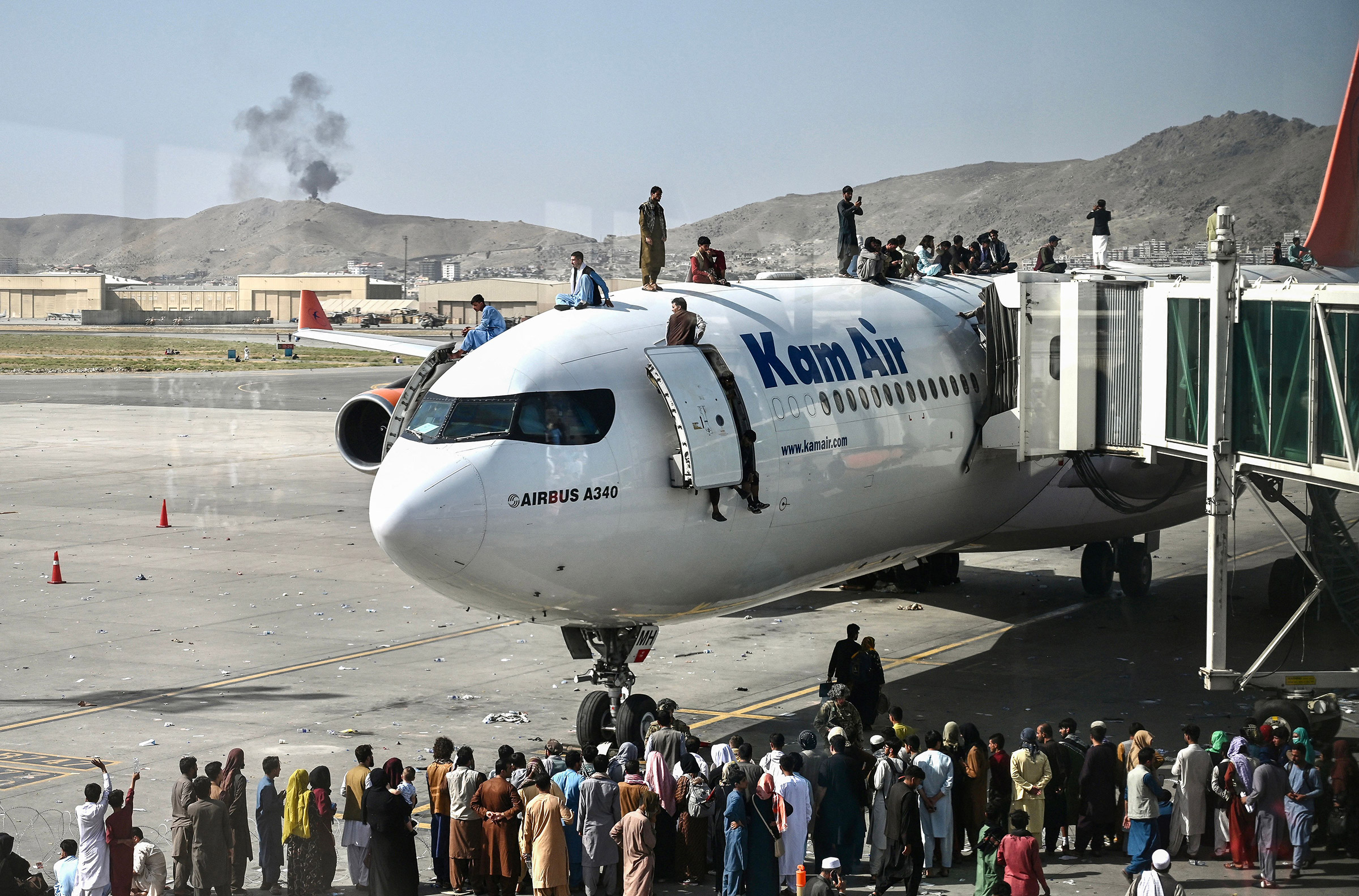 Afghan people climb atop a plane as they wait at the Kabul airport in Kabul on Aug. 16, 2021.