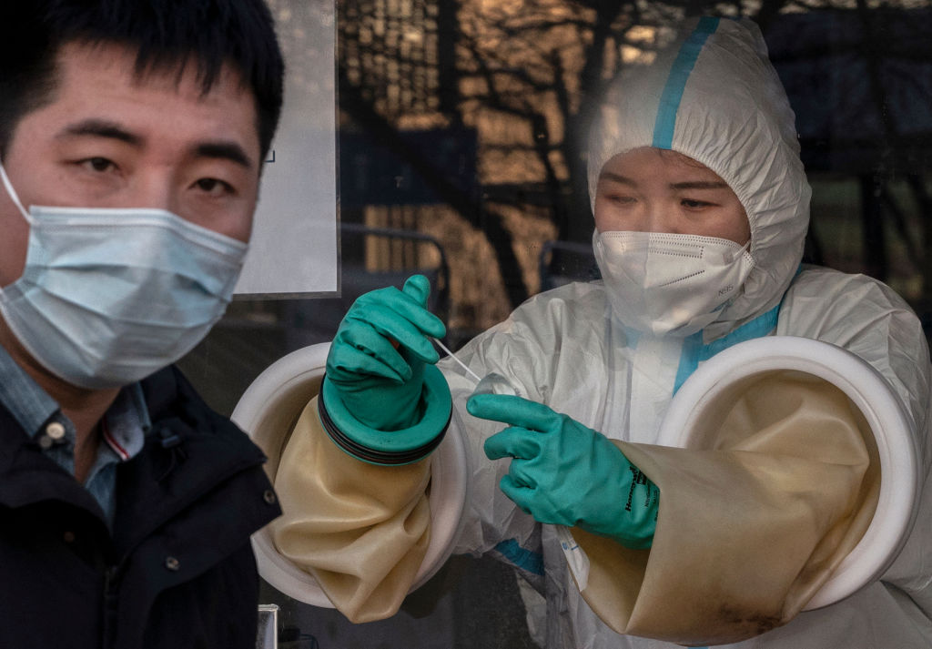 A medical worker reaches through protective gloves as she places a swab back in its case after administering a nucleic acid test to a client at a private outdoor clinic on December 27, 2021 in Beijing, China. (Kevin Frayer/Getty Images)