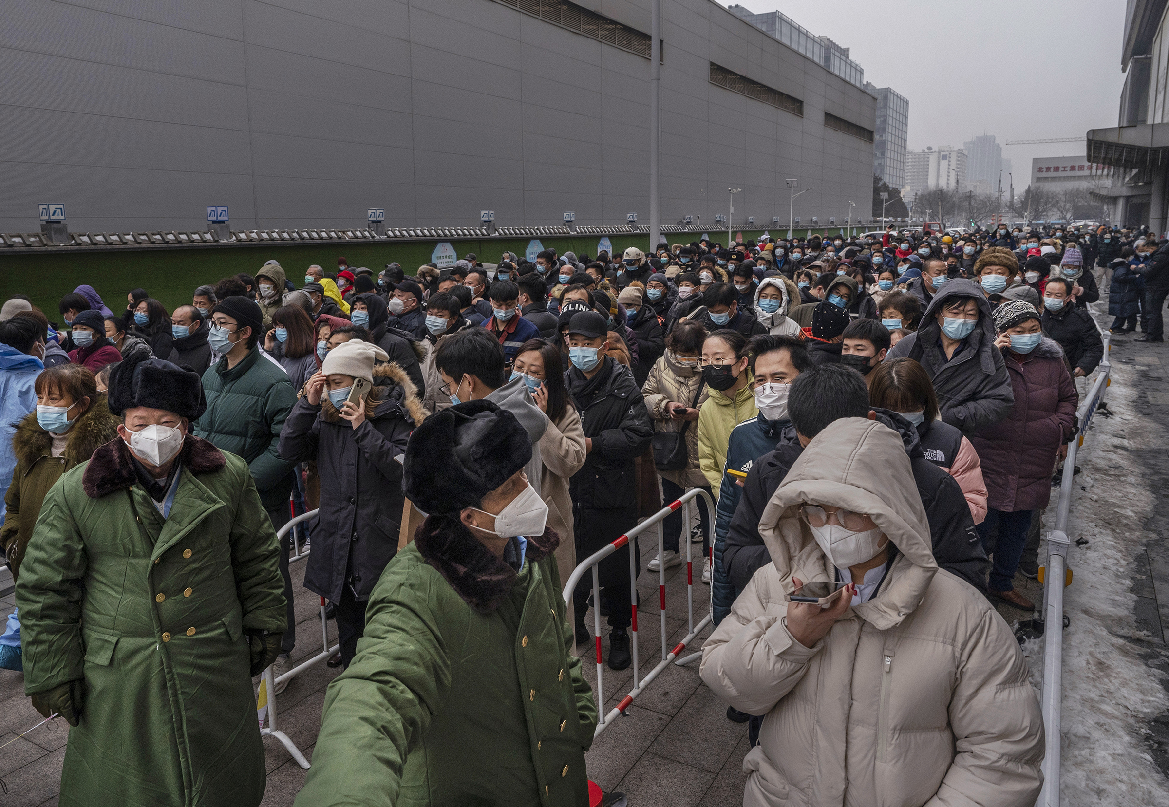 Security stand in front of people as they line up for nucleic acid tests to detect COVID-19 at a mass testing site on January 24, 2022 in Beijing, China. While China has mostly contained the spread of COVID-19 during the pandemic, and even though cases remain relatively low, recent outbreaks of the virus including the emergence of the highly contagious Omicron variant have prompted the government to lockdown people in various major cities and to reinforce stricter health measures. Mask mandates, mass testing, immunization boosters, quarantines, some travel restrictions and bans and lockdowns have become the norm as China continues to maintain its zero-COVID policy. (Kevin Frayer—Getty Images)