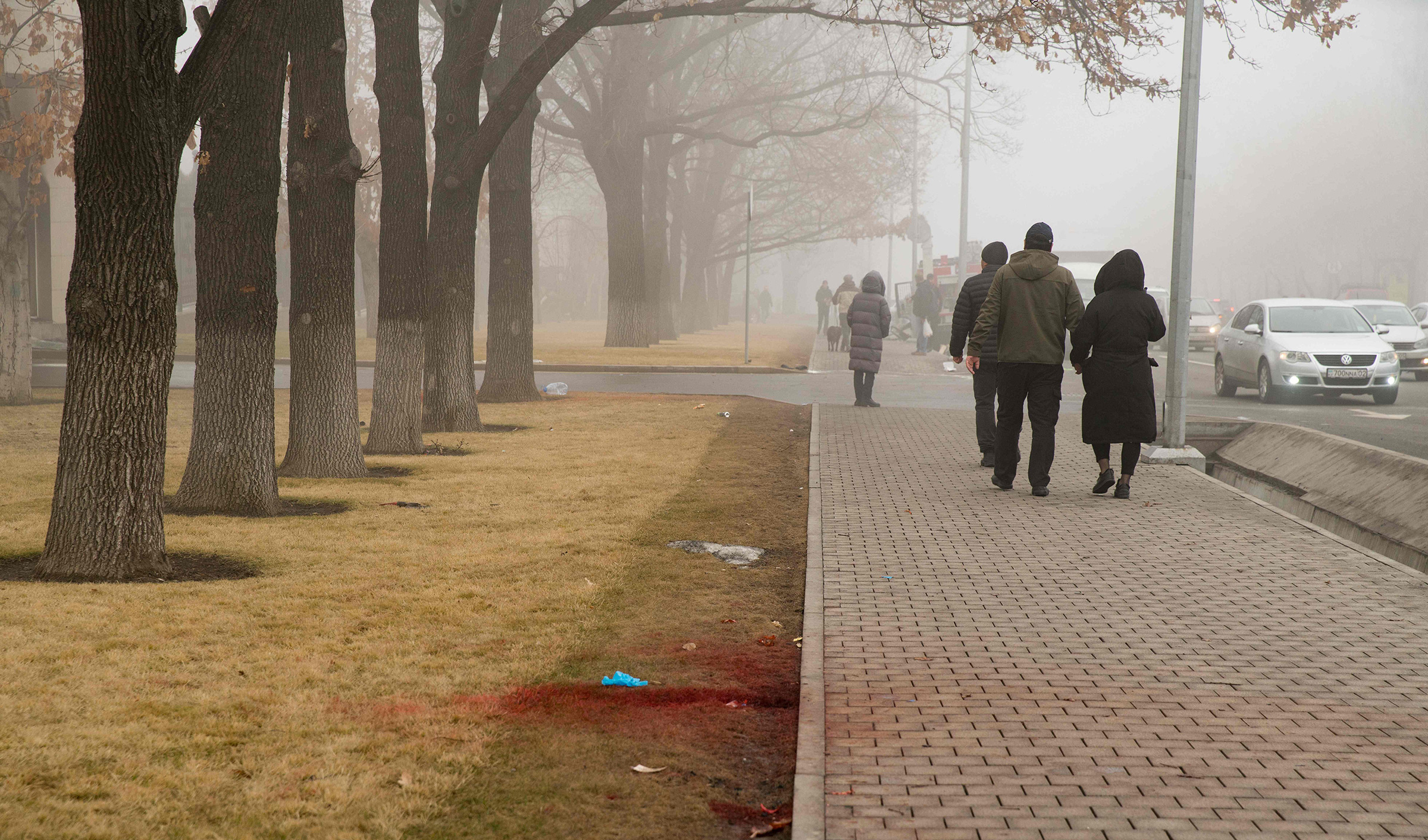 People walk past blood on a curbside lawn after violence that erupted following protests over hikes in fuel prices, in Almaty, Kazakhstan on Jan. 6, 2022. (Alexander Bogdanov— AFP/Getty Images)