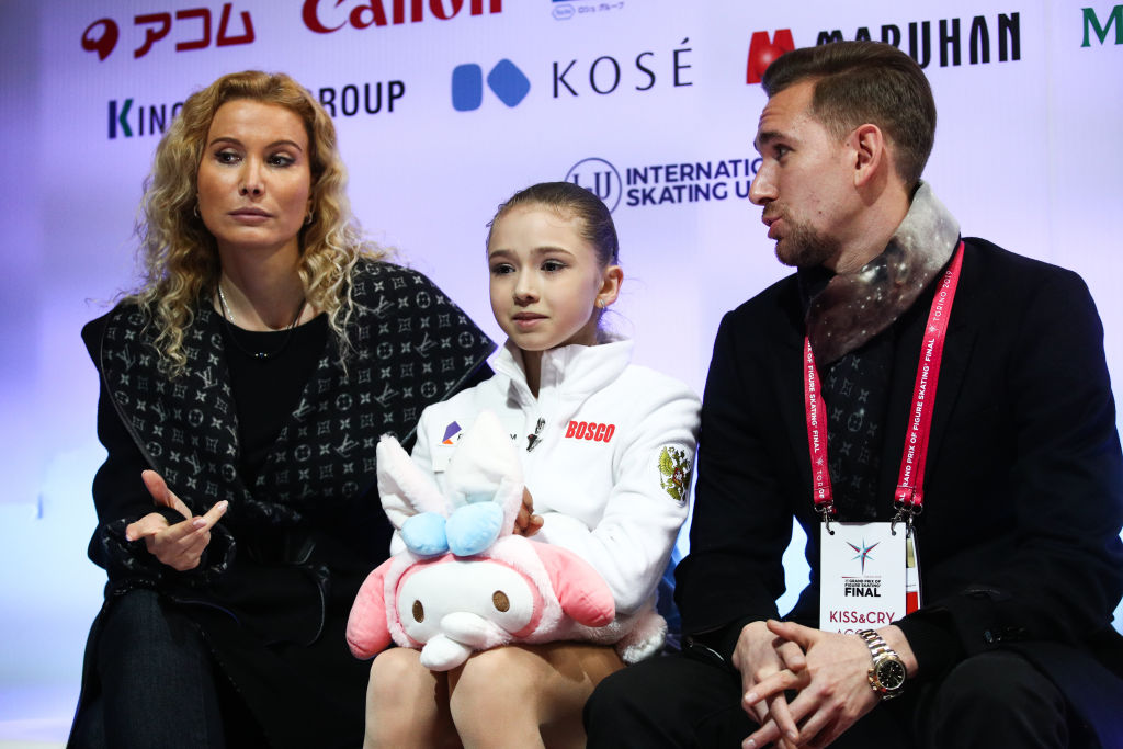 Figure skater Kamila Valieva (C) of Russia with her coaches Eteri Tutberidze (L) and Daniil Gleikhengauz (R) waiting for the score after performing during a ladies' free skating event at the 2019-20 ISU Junior Grand Prix of Figure Skating Final, at the Torino Palavela indoor arena. (Sergei Bobyle—TASS via Getty Images)