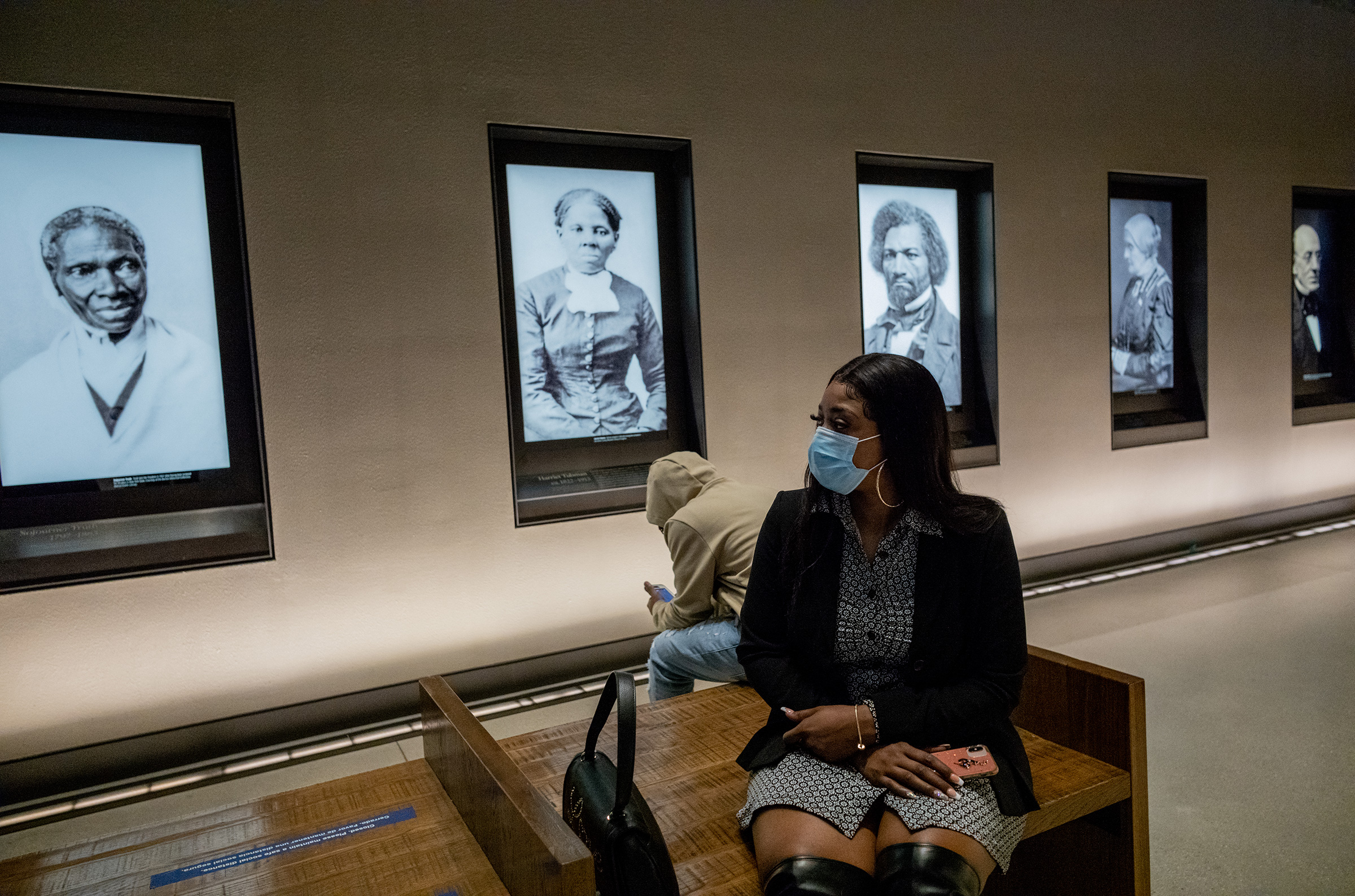 Bridgett Floyd sits near a wall showing famous portraits at the National Museum of African American History and Culture on Feb. 27 in Washington, D.C. She is flanked by digitized photographs of Harriet Tubman and Frederick Douglass. (Ruddy Roye for TIME)