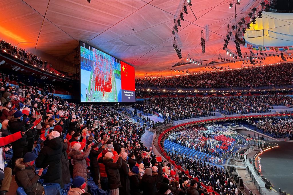 Spectators wave China's national flags as they watch from the stands while Chinese athletes take part in the parade of delegations during the opening ceremony of the Beijing 2022 Winter Olympic Games, at the National Stadium in Beijing, on Feb. 4, 2022. (MATTHEW WALSH/AFP via Getty Images)