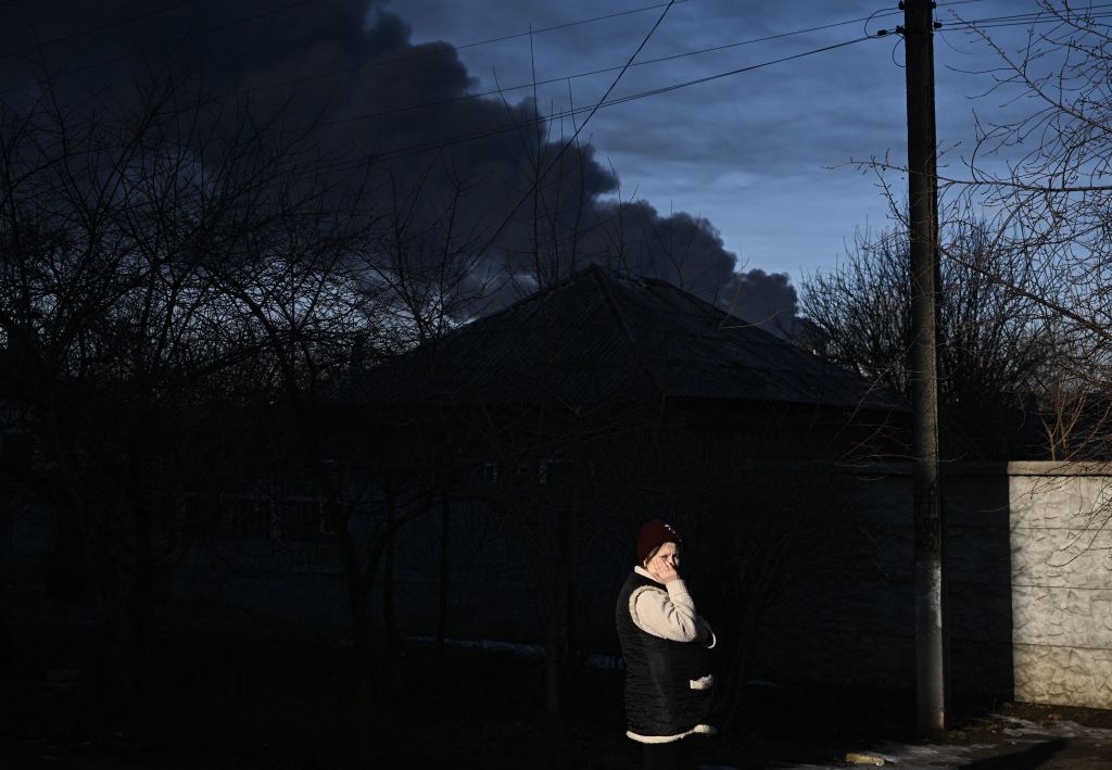 A woman stands in a street as black smoke rises from a military airport in Chuguyev near Kharkiv on Feb. 24, 2022. (AFP via Getty Images)