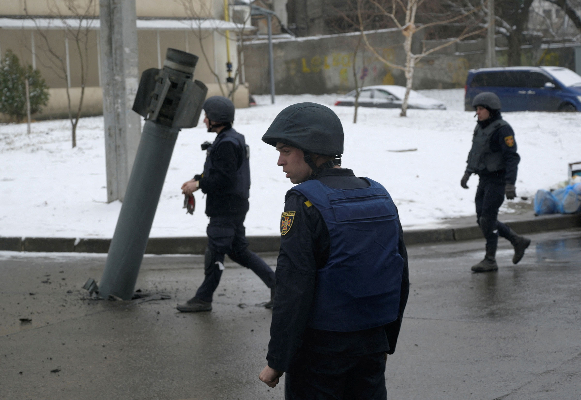 Members of the State Emergency Service of Ukraine walk towards a rocket case stuck in pavement following a recent shelling in Kharkiv on Feb. 25. (Maksim Levin—Reuters)
