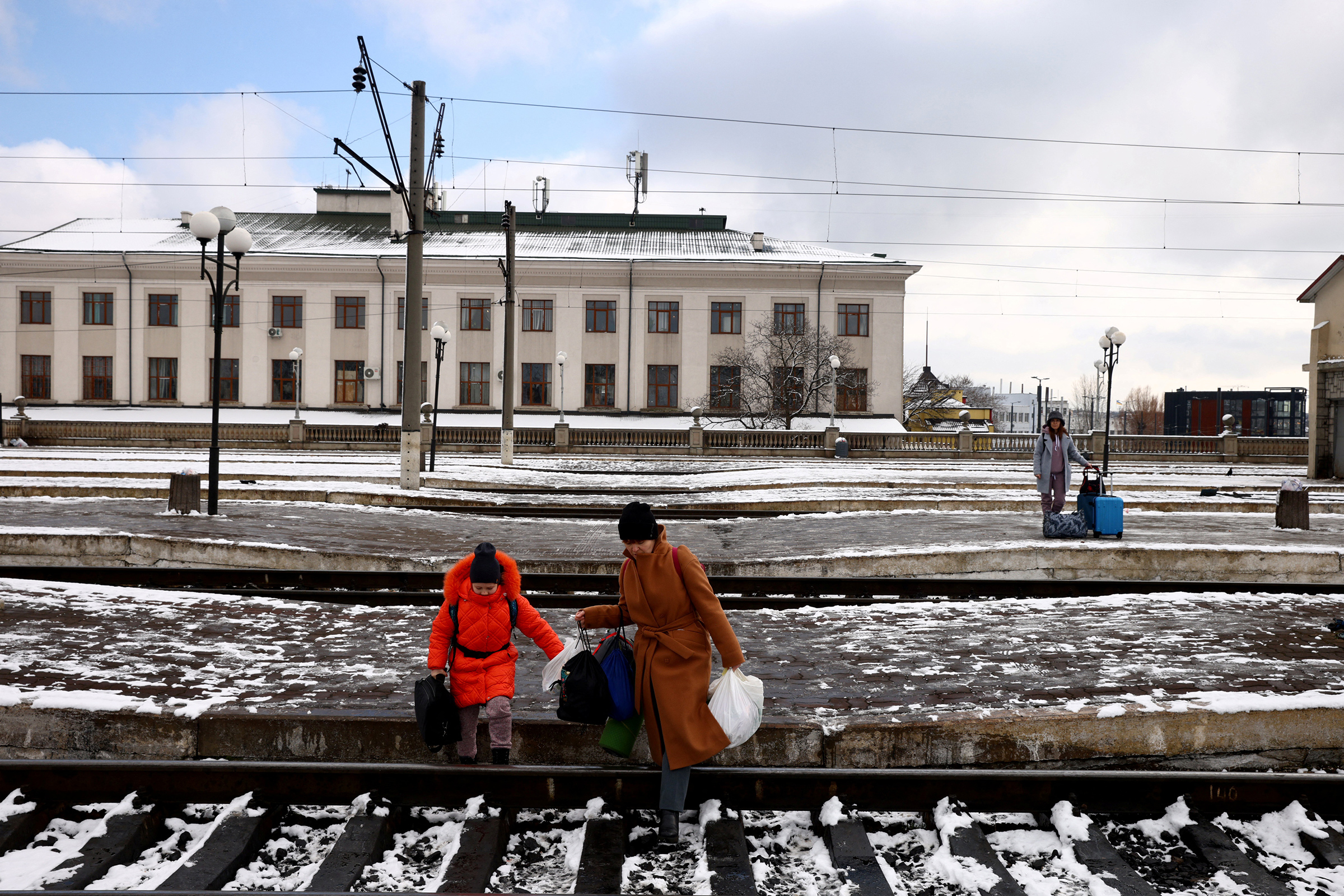 People fleeing Russia's invasion of Ukraine cross train tracks to get to a train leaving for Poland at the train station in Lviv, Ukraine, on Feb. 28 (Thomas Peter—Reuters)
