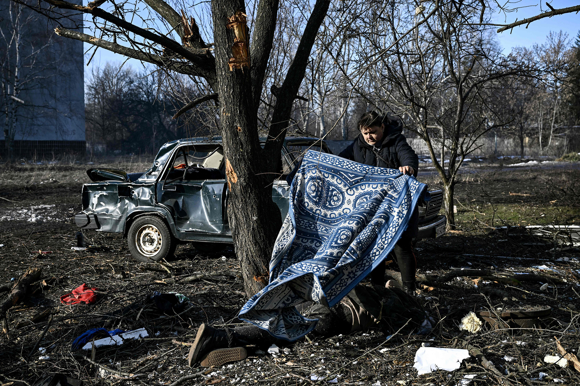 A man uses a carpet to cover a body on the ground after bombings on the eastern Ukraine town of Chuguiv on Feb. 24. Russia's ground forces today crossed into Ukraine from several directions, Ukraine's border guard service said, hours after President Vladimir Putin announced the launch of a major offensive.