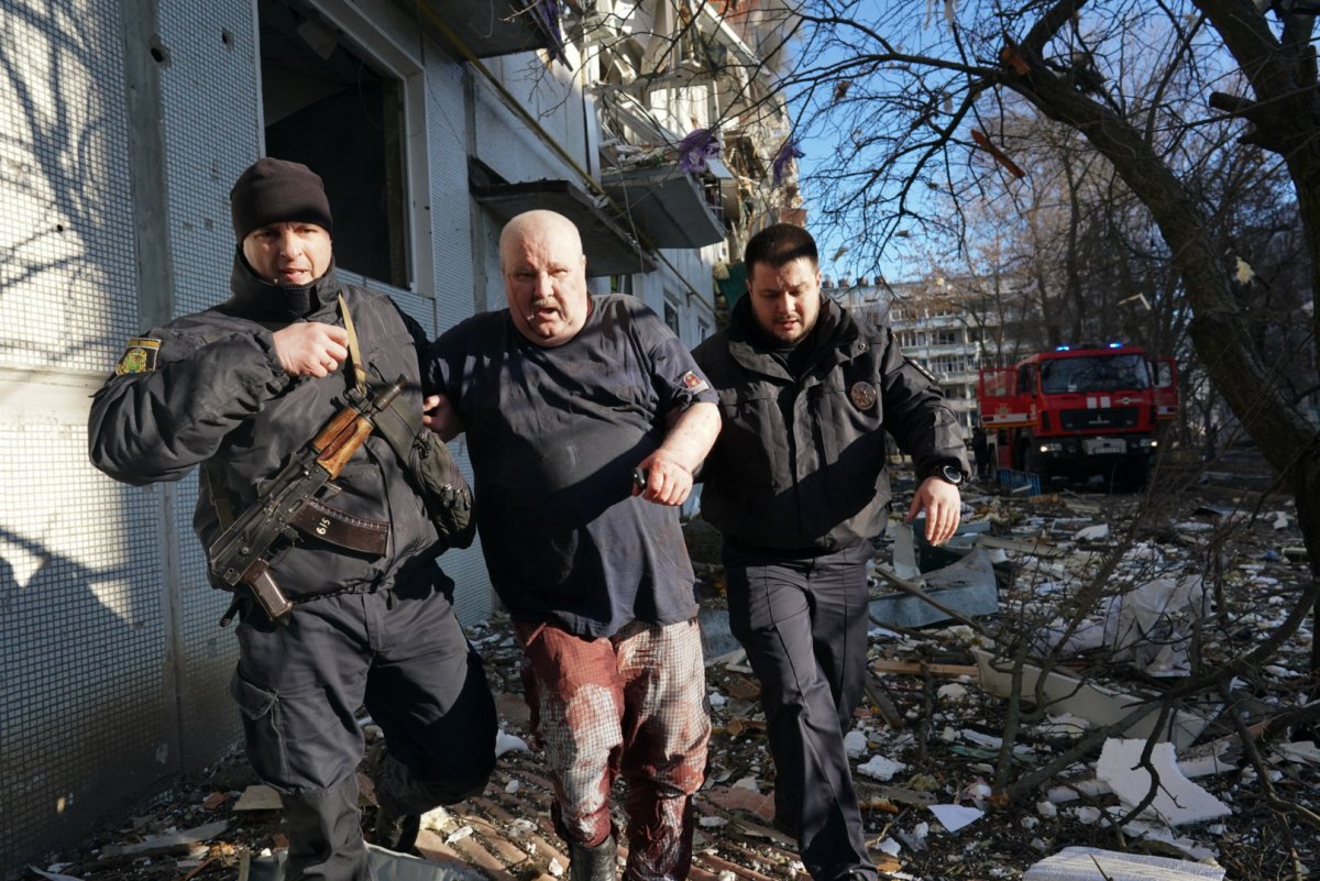Lực lượng an ninh Ukraine tháp tùng một người đàn ông bị thương sau khi một cuộc không kích tấn công một khu chung cư ở Chuhuiv, Kharkiv Oblast vào ngày 24 tháng 2. Wolfgang Schwan — Anadolu Agency / Getty Images