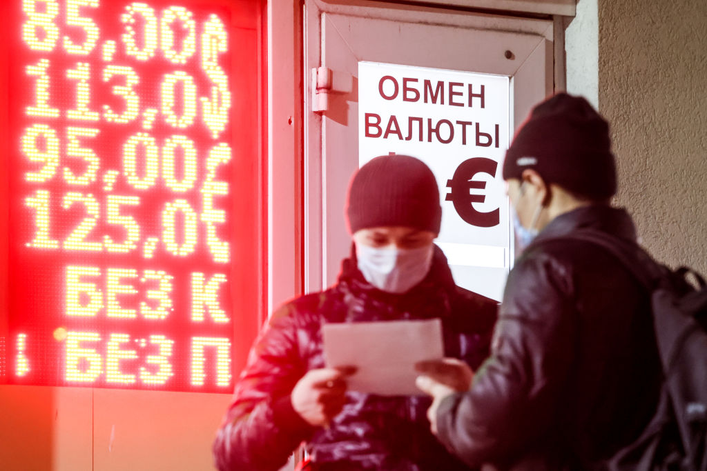 Men are seen by a board showing Russian rouble exchange rates, outside a currency exchange office in Moscow on Mar. 2, 2022. (Mikhail Metzel/TASS)