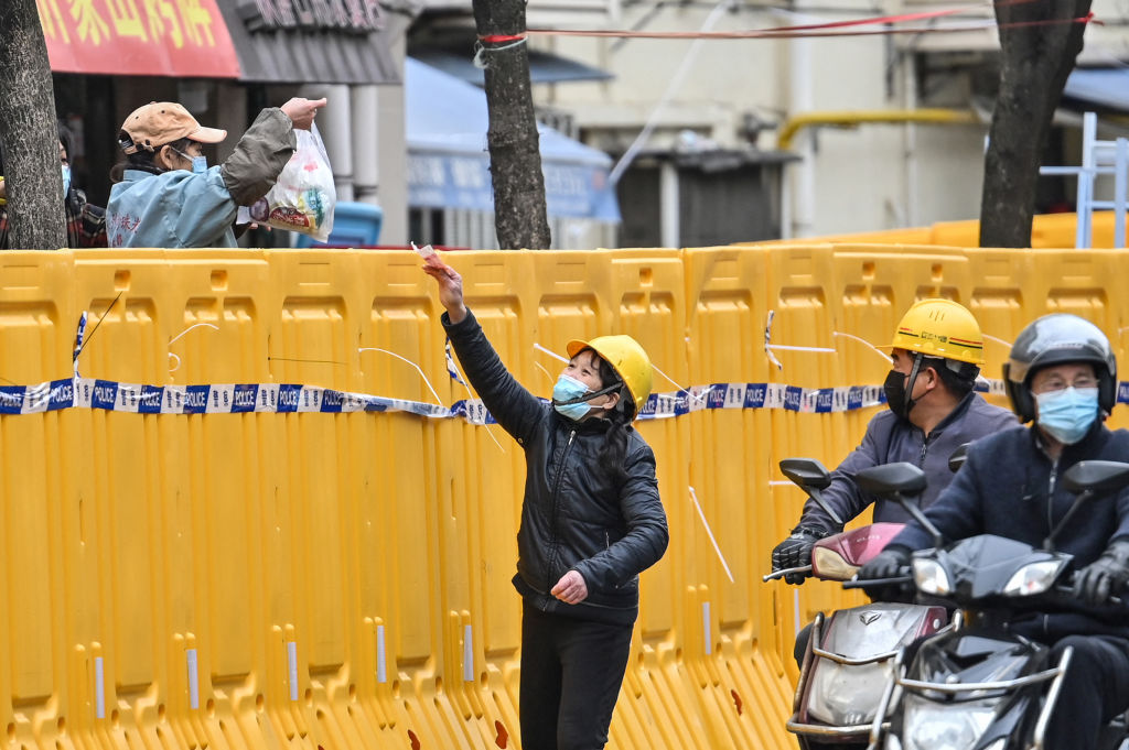 A woman (L) in lockdown sells goods from behind barriers during lockdown as a measure against the Covid-19 coronavirus in Jing'an district, in Shanghai on March 31, 2022. (Hector RETAMAL-AFP)