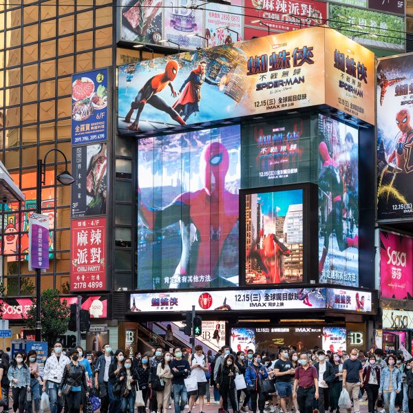 People are seen crossing the street as advertisement billboard screens from Marvel comics character Spider-Man  No Way Home movie, co-produced by Columbia Pictures and distributed by distributed by Sony Pictures, are being displayed above them in Hong Kong.