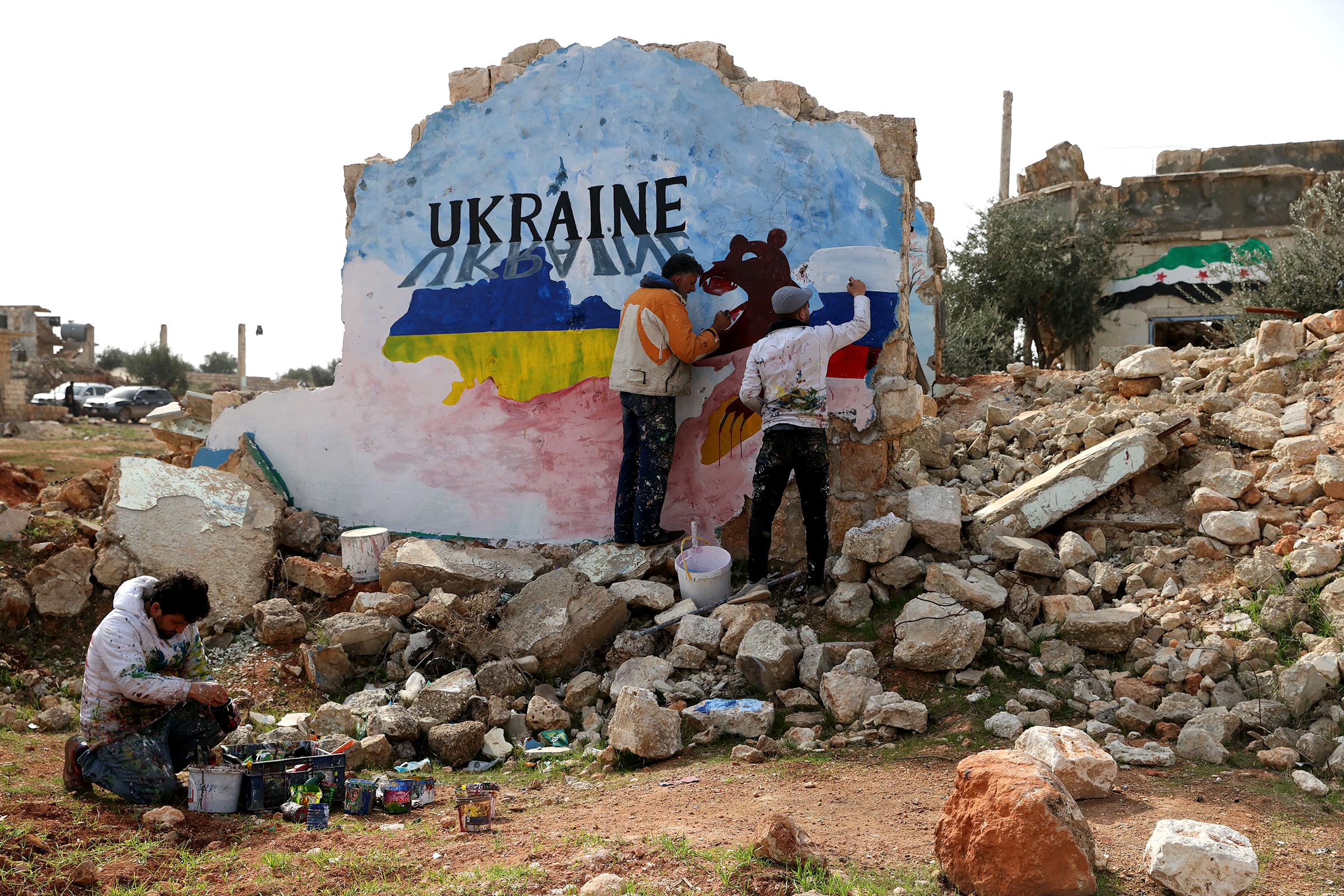 Syrian artists Aziz Asmar and Anis Hamdoun paint a mural amid the destruction, depicting the colours of the Russian and Ukrainian flags, to protest against Russia's military operation in Ukraine, in the rebel-held town of Binnish in Syria's northwestern Idlib province on February 24, 2022. (Omar Haj Kadour—AFP/Getty Images)