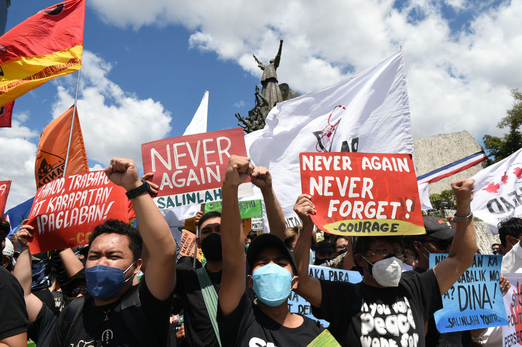 Protesters raise clinched fists as they hold banners with anti-Marcos slogans during a demonstration to commemorate the 36th anniversary of the People Power Revolution in 1986 that ousted the late dictator Ferdinand Marcos, in front of the People Power monument in Quezon City, suburban Manila on Feb. 25, 2022. (Ted Aljibe—AFP/Getty Images)