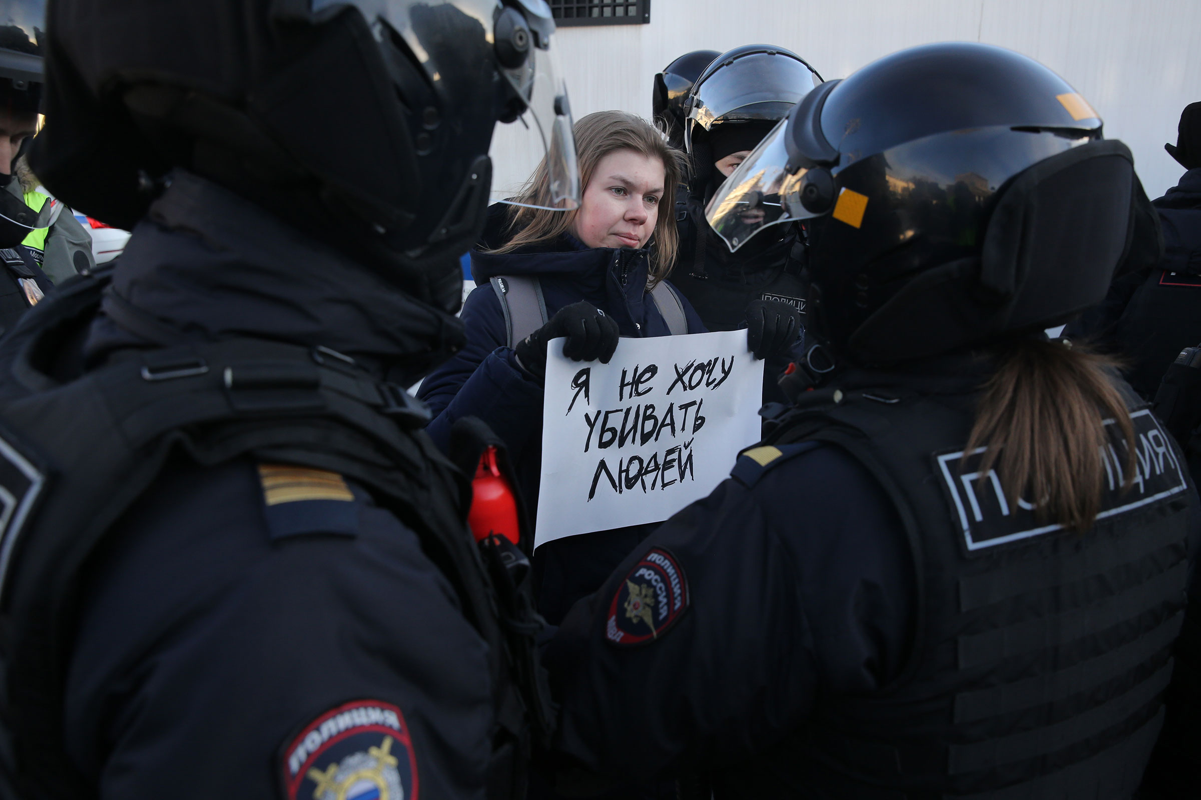 Russian Police officers detain a woman holding a poster that reads: 